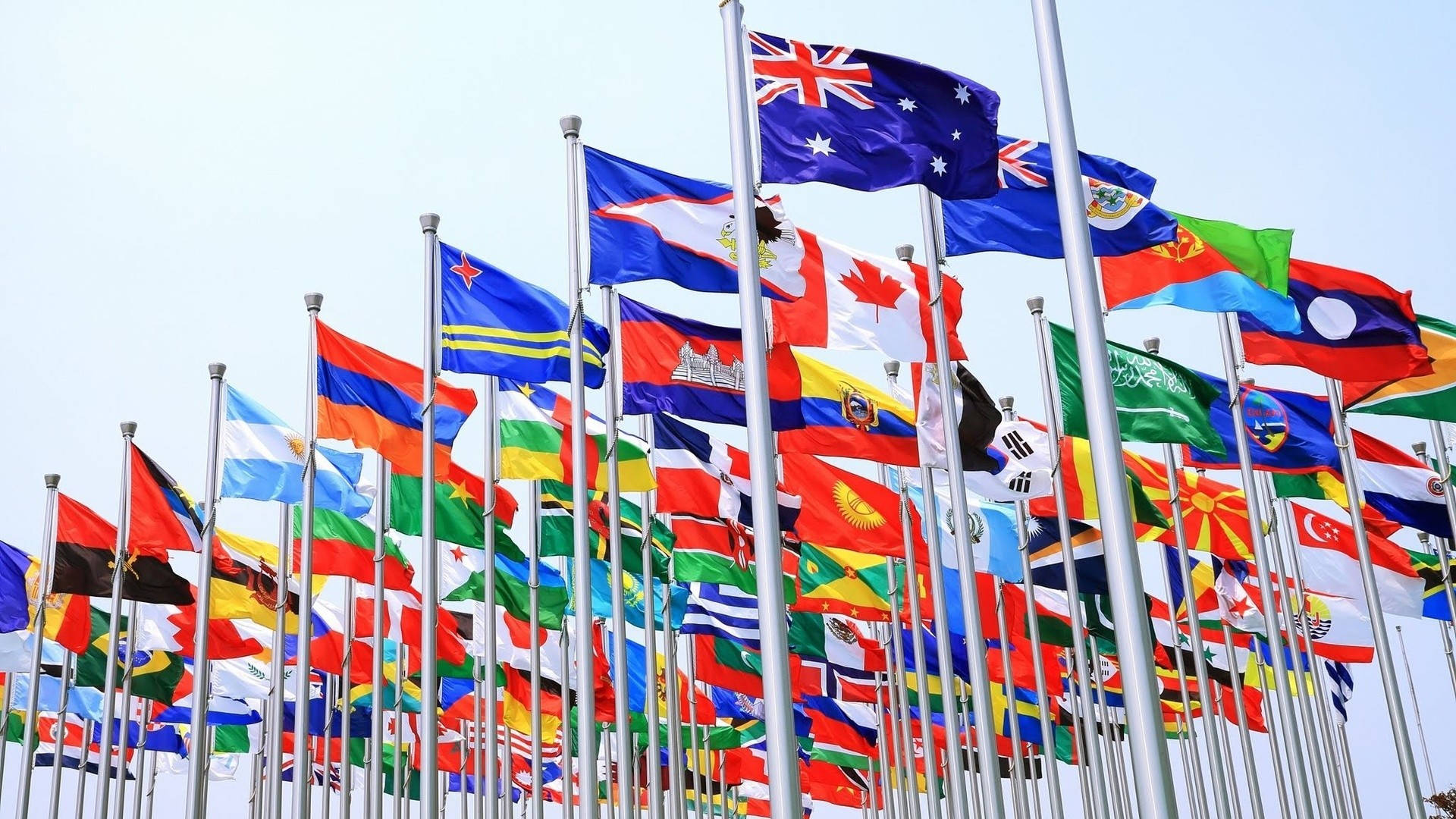World 桌布 壁紙 — 一組鮮豔的國際旗幟在晴朗的藍天下整齊地飄揚。