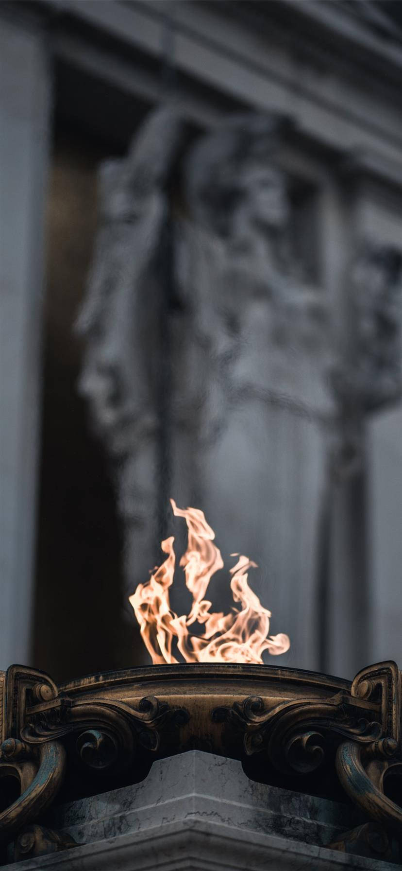 iPhone Fire 桌布 壁紙 — 一縷充滿活力的火焰在華麗的青銅火盆上舞動，背景是模糊的石像。