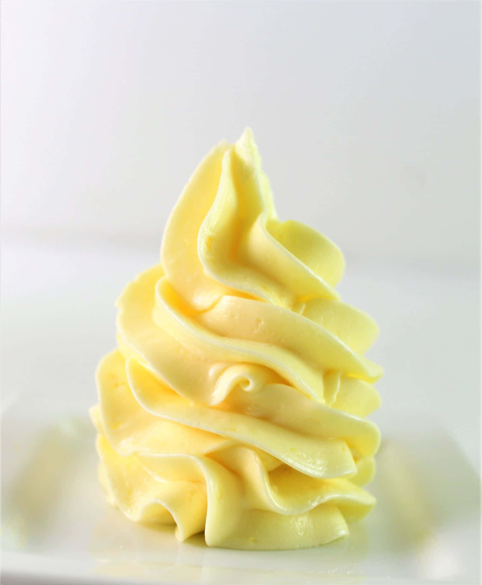 Buttercream 桌布 壁紙 — 一縷完美的淡黃色鮮奶油優雅地放在白色盤子上，背景柔和模糊。