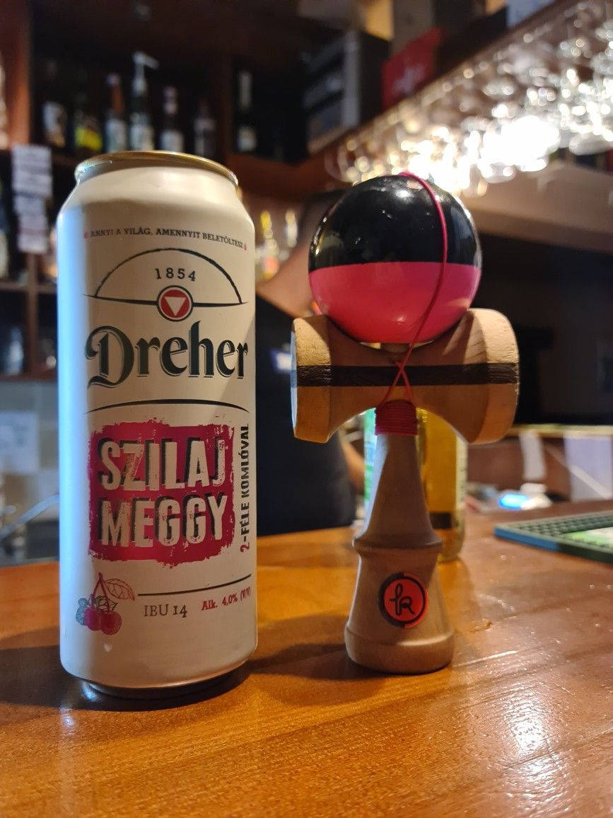 alcohol 桌布 壁紙 — 一罐Dreher櫻桃味啤酒放在舒適酒吧的溫暖木吧檯上，旁邊有一個木製劍玉玩具。