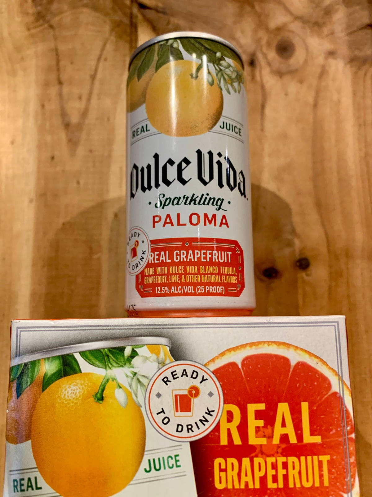 cocktail 桌布 壁紙 — 一罐Dulce Vida Sparkling Paloma和一盒真正的葡萄柚汁放在溫暖的木質表面上。