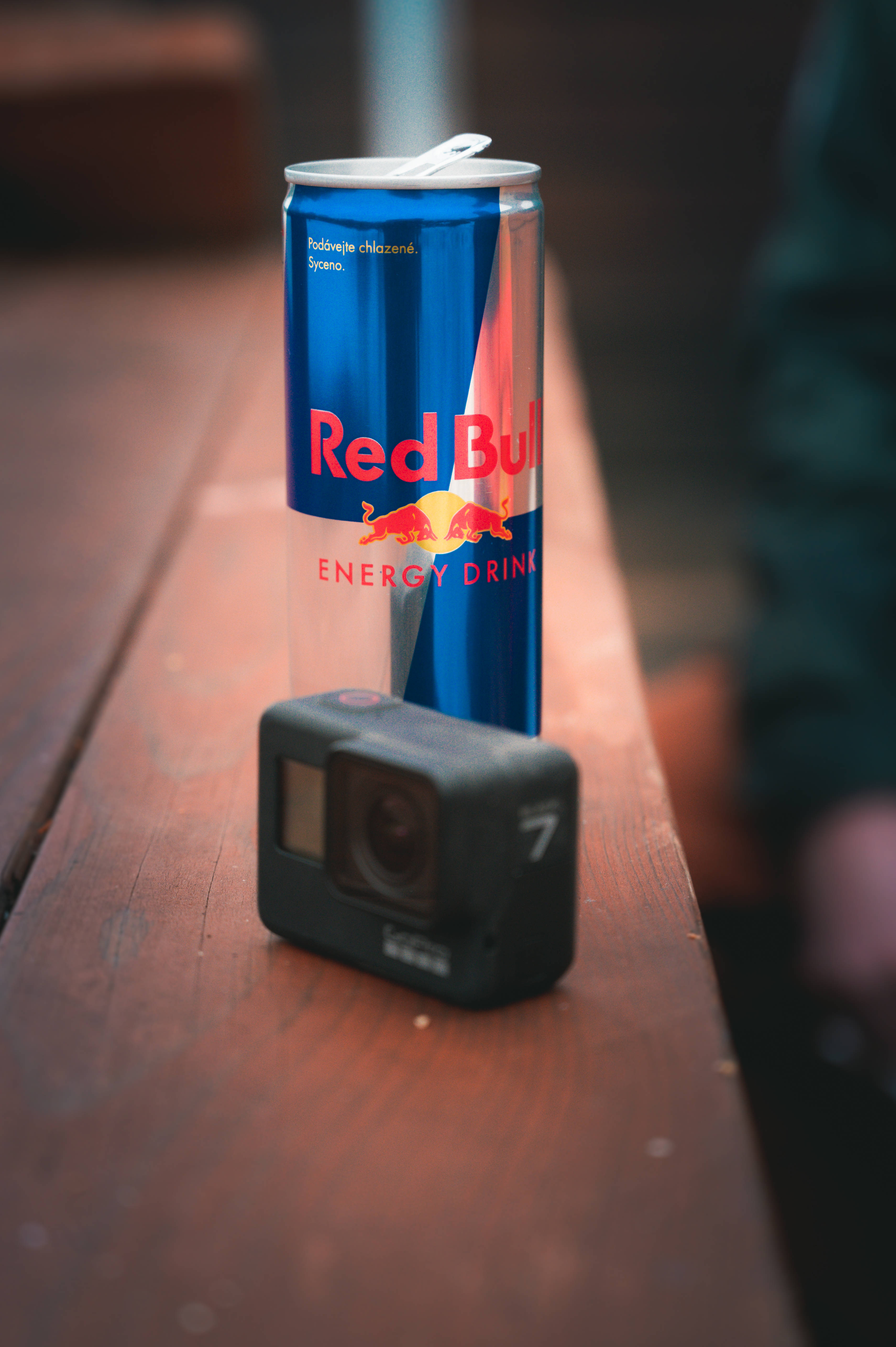 bull 桌布 壁紙 — 一罐Red Bull能量飲料和一台GoPro相機並排放在木質表面上，景深較淺。