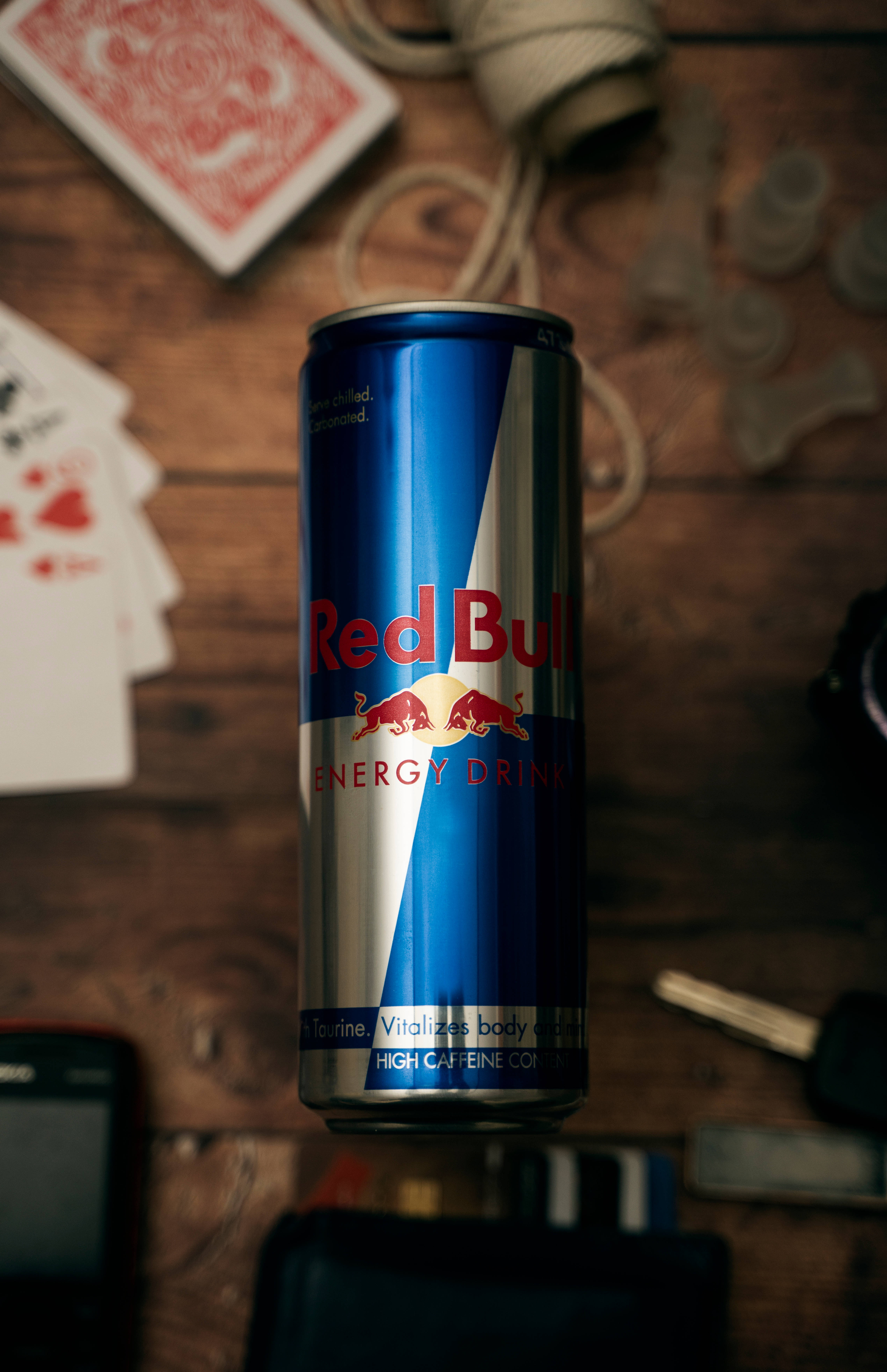 bull 桌布 壁紙 — 一罐Red Bull能量飲料放在鄉村風木桌中央，周圍散落著撲克牌、鑰匙和相機。