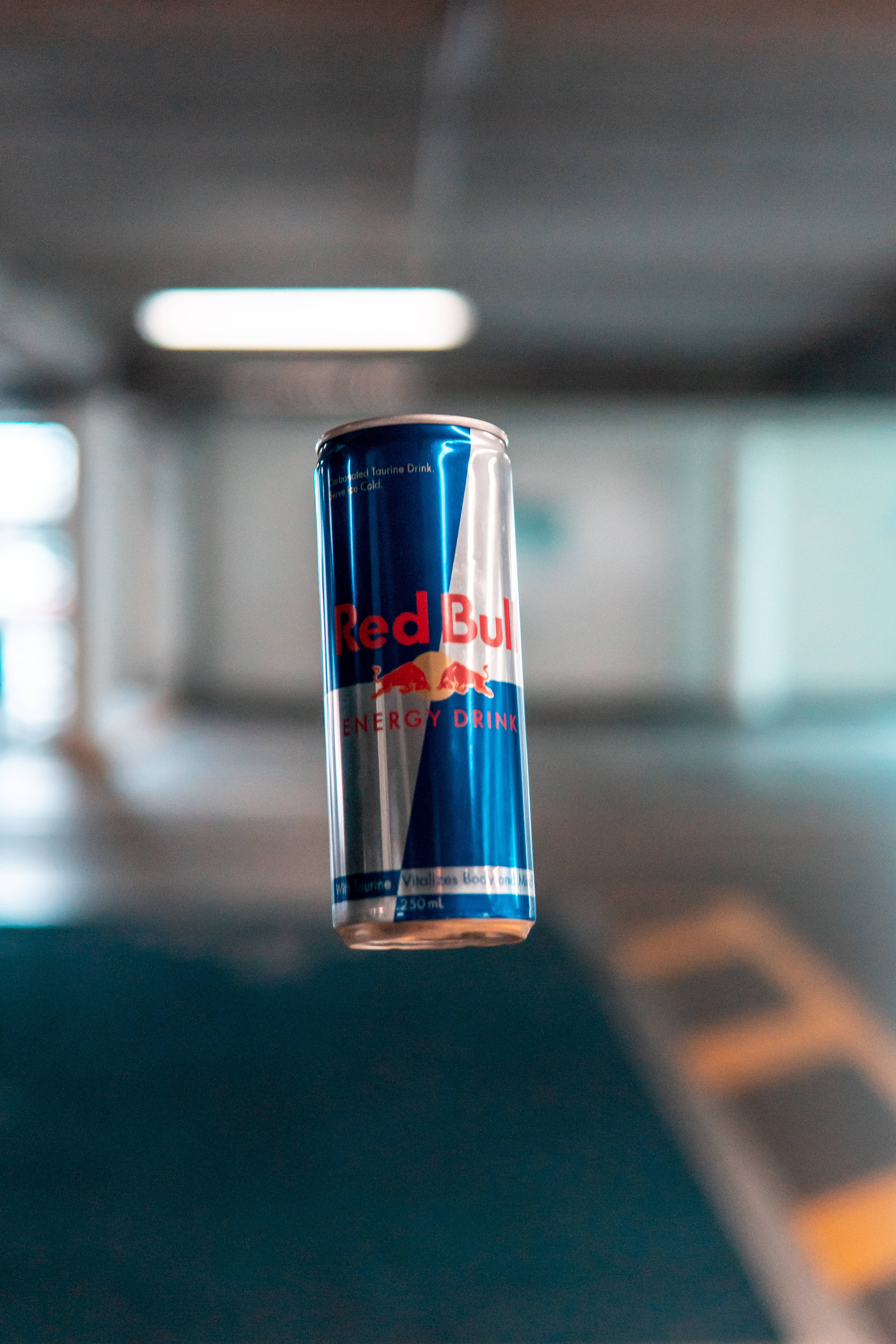bull 桌布 壁紙 — 一罐Red Bull能量飲料罐在半空中漂浮，位於燈光昏暗的地下停車場，帶有模糊的螢光燈。