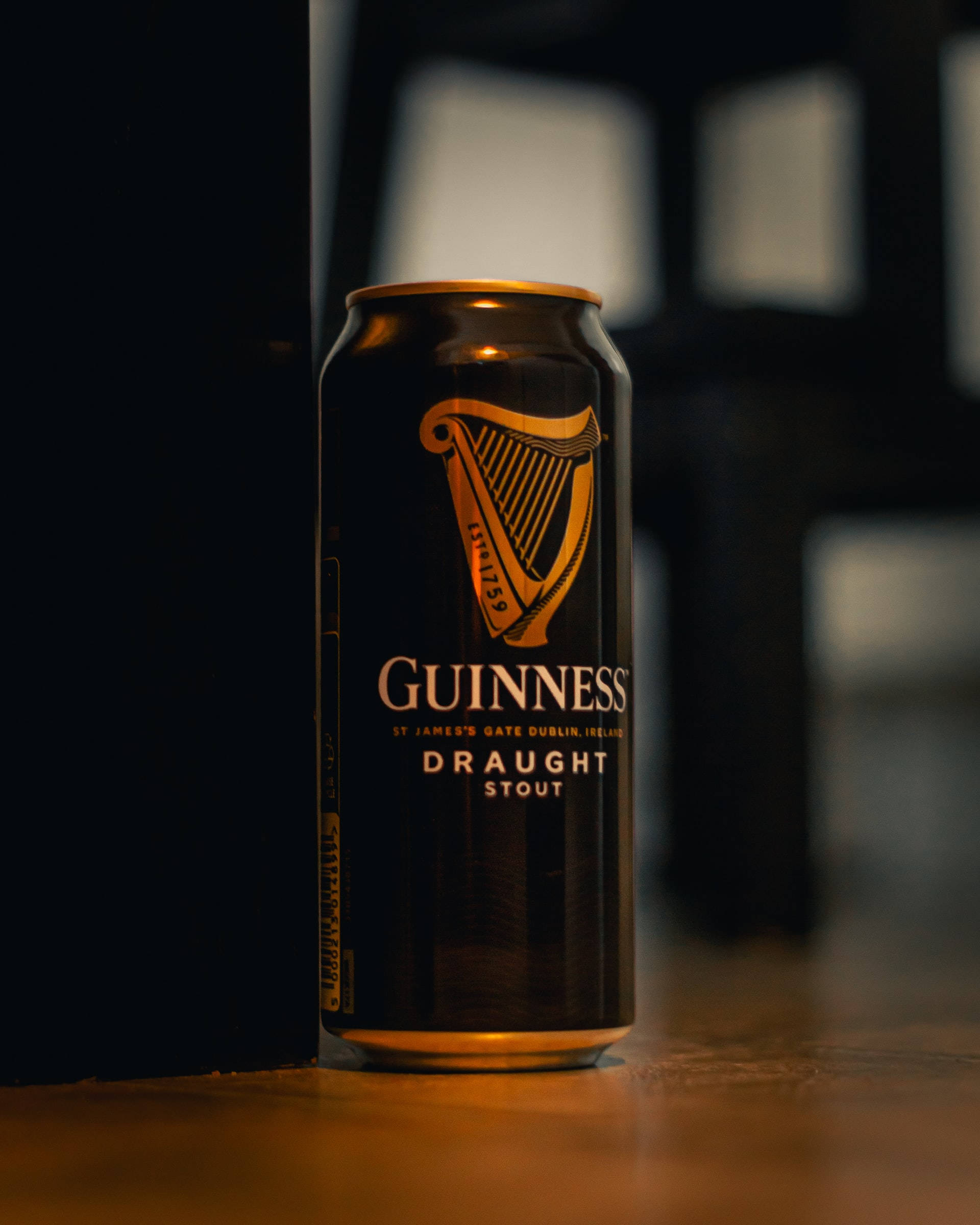 Beer 桌布 壁紙 — 一罐健力士黑啤直立於木質表面上，沐浴在溫暖的金色光線中，背景為深色模糊。
