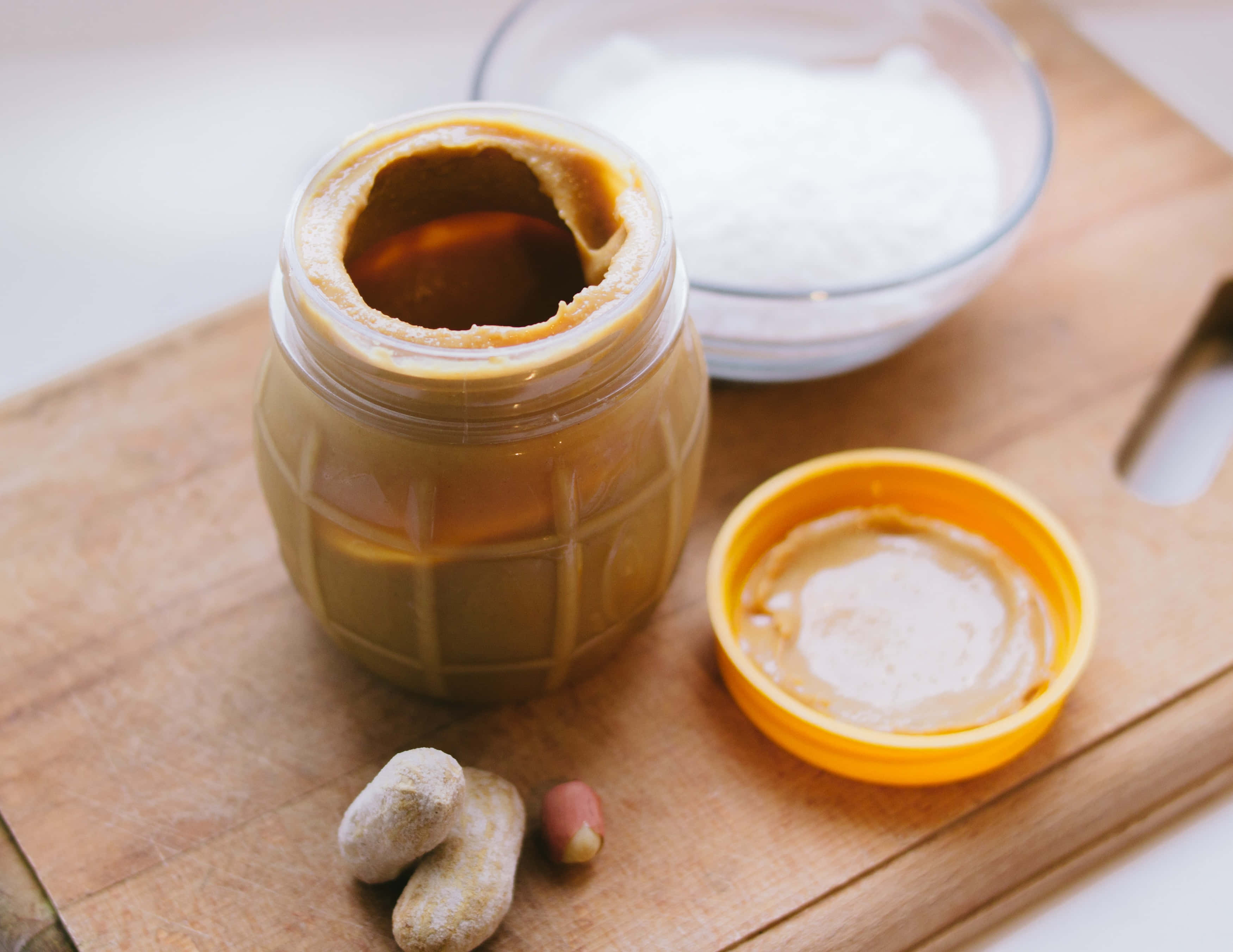 Caramel 桌布 壁紙 — 一罐幼滑花生醬打開放在木砧板上，旁邊有原粒花生和一碗糖。