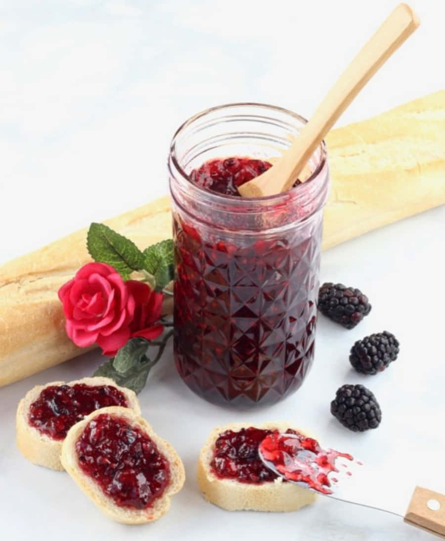 Blackberry Jam 桌布 壁紙 — 一罐閃亮的黑莓果醬配木勺，旁邊放著塗有果醬和新鮮莓果的法國麵包片。