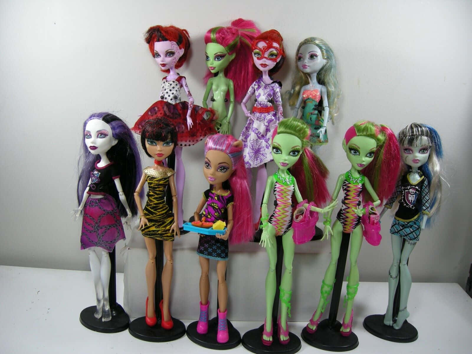 Dolls 桌布 壁紙 — 一群Monster High公仔，擁有色彩繽紛的頭髮和哥德式服裝，在黑色支架上擺姿勢，背景是純白色牆壁。
