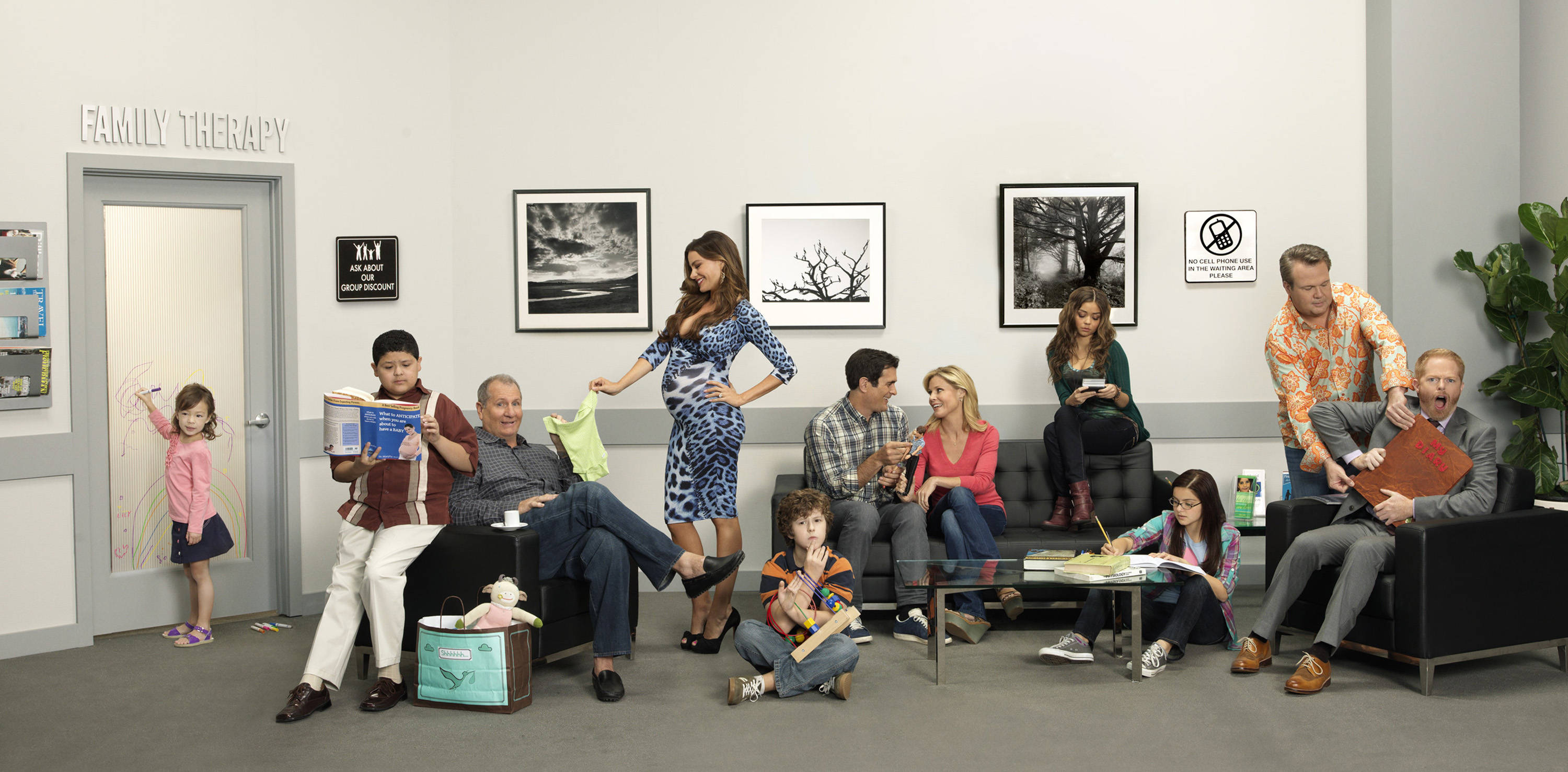 Modern Family 桌布 壁紙 — 一群不同背景的人，包括兒童和成人，坐在或站在標有「家庭治療」的候診室中，牆上掛著裱框的黑白藝術品。