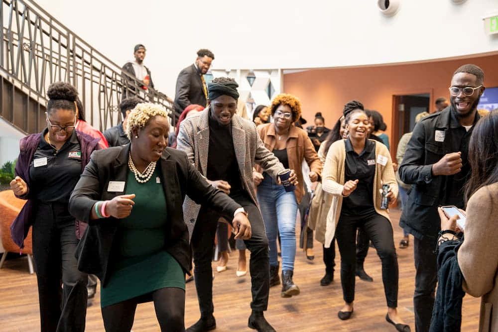 Black Culture 桌布 壁紙 — 一群不同背景的人快樂地在一個現代化的室內空間中充滿活力地跳舞，該空間鋪有木地板並設有欄杆。