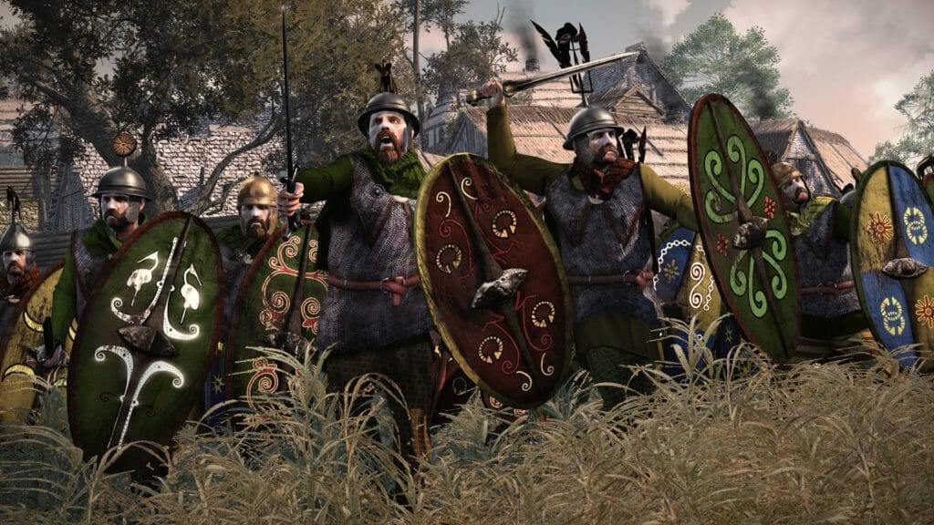 rome 2 桌布 壁紙 — 一群中世紀戰士，手持華麗盾牌，頭戴裝飾頭盔，站在村莊附近的高草叢中，準備戰鬥。
