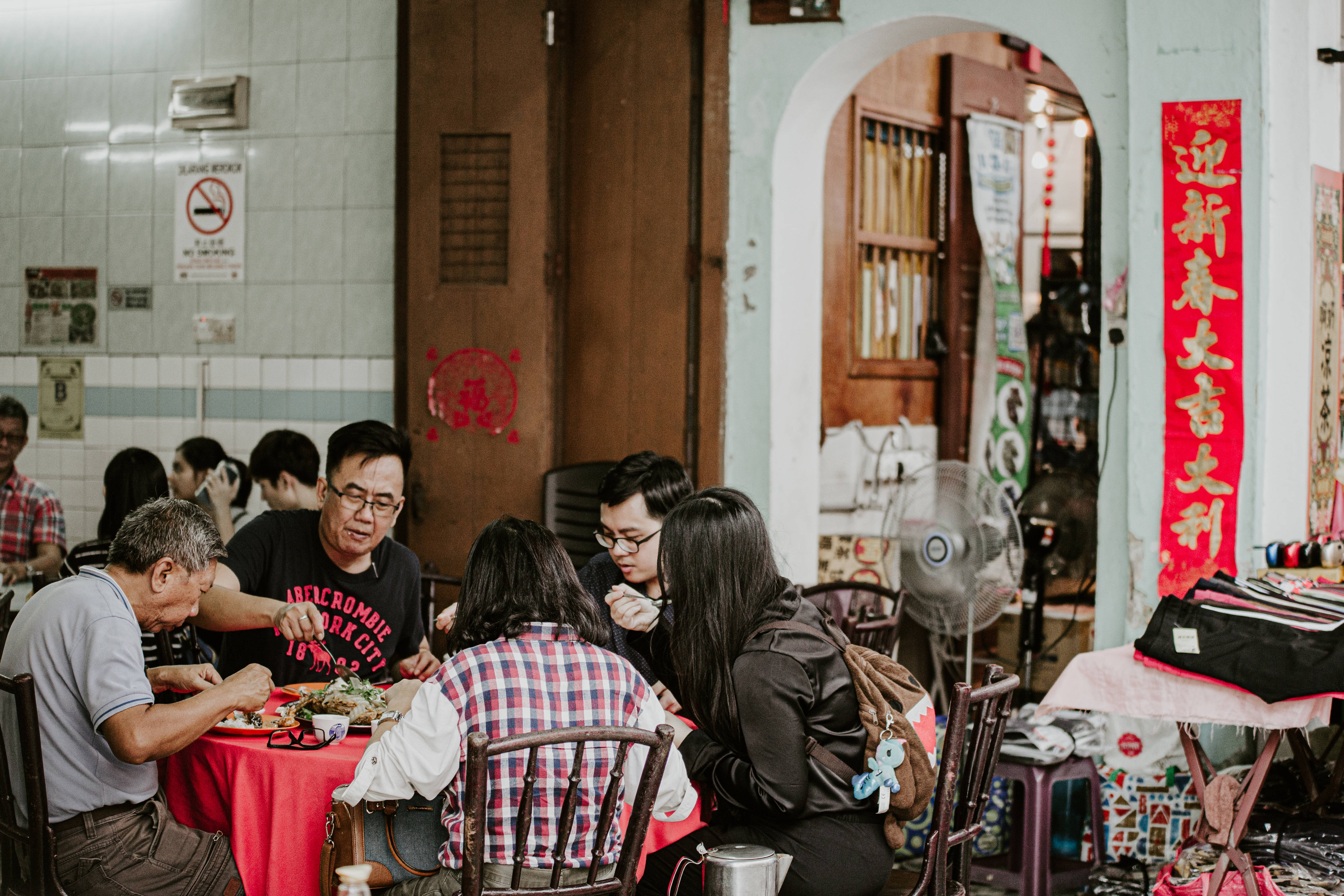 春節 桌布 壁紙 — 一群人在一家熱鬧的本地餐廳共享一頓飯，餐廳鋪有紅色桌布並掛有農曆新年裝飾。