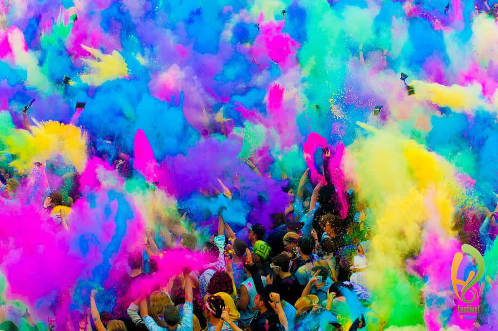 Holi 桌布 壁紙 — 一群人群歡樂地將鮮豔的彩色粉末拋向空中，創造出粉紅、藍、黃、綠色的耀眼爆炸。