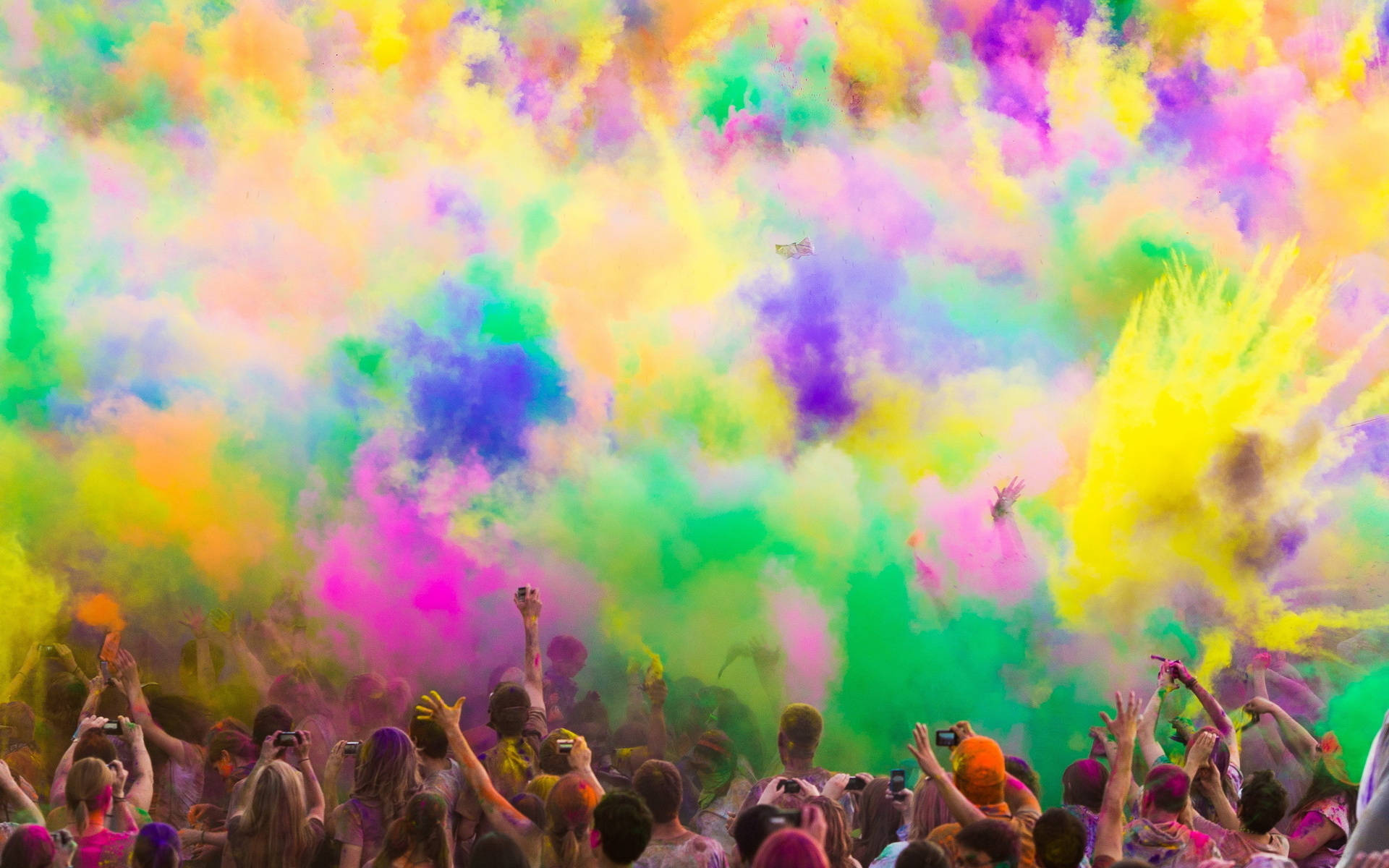 Holi 桌布 壁紙 — 一群人群歡樂地將鮮豔的彩色粉末拋向空中，在他們上方創造出令人眼花撩亂的色彩爆炸。