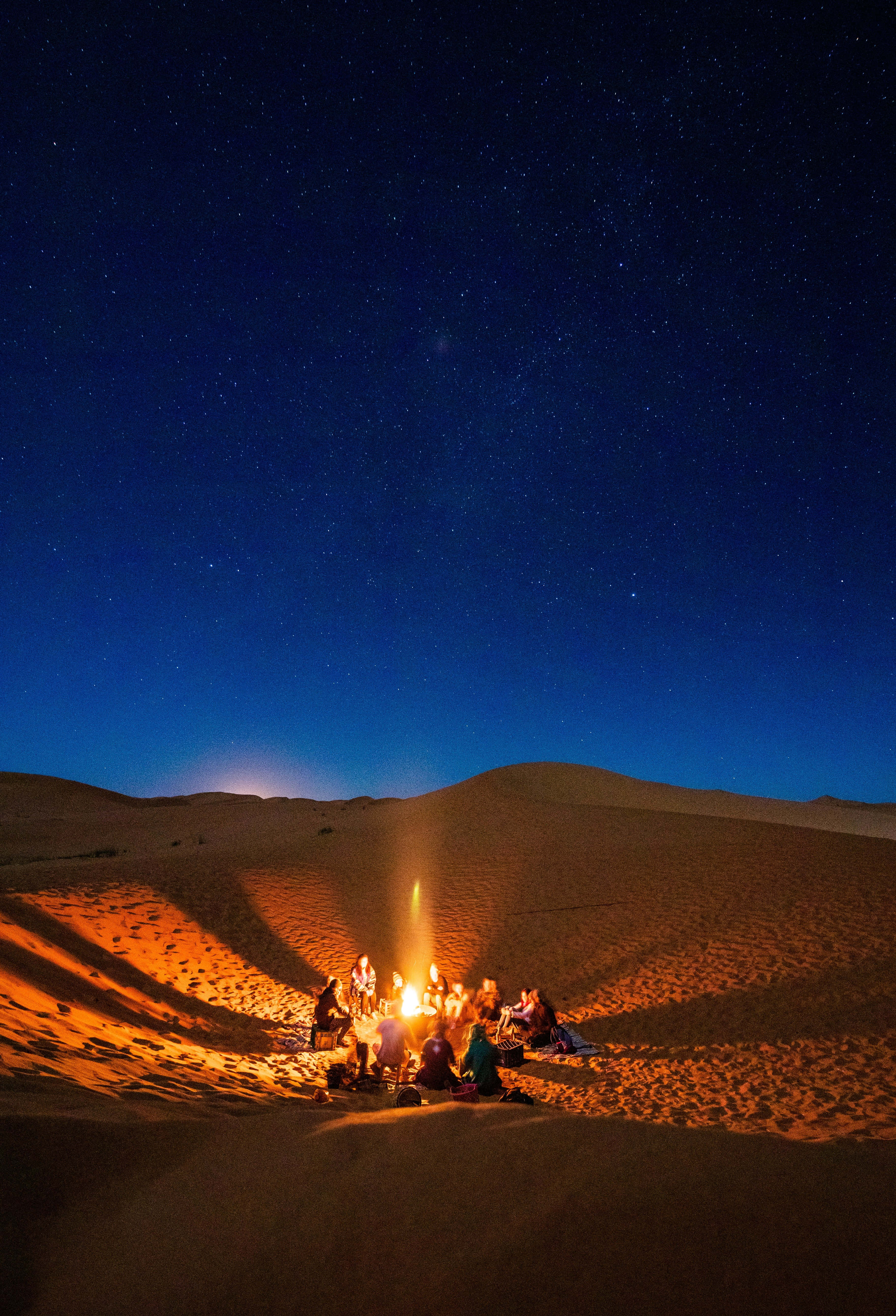 Bonfire 桌布 壁紙 — 一群人聚集在溫暖的營火旁，身處沙漠夜晚廣闊的星空下。