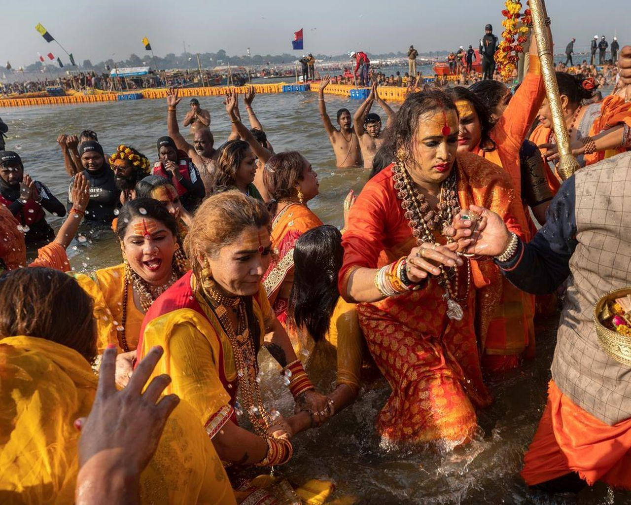 Indian 桌布 壁紙 — 一群充滿活力、身穿橙色和黃色傳統服飾的人群，在宗教節日期間歡樂地浸入聖河。
