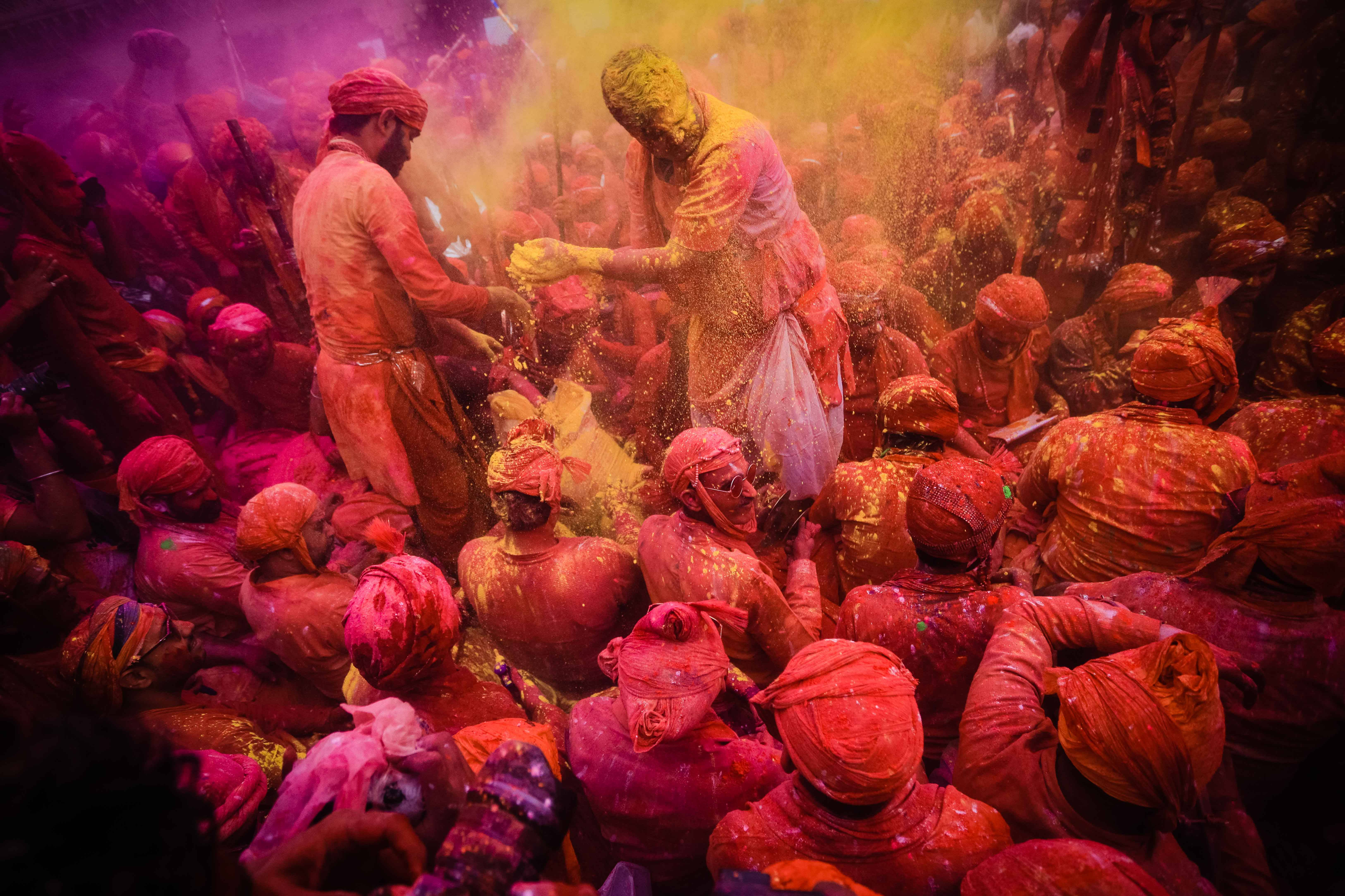 Holi 桌布 壁紙 — 一群充滿活力的人們身上沾滿紅色和黃色粉末，在旋轉的色彩爆炸中慶祝灑紅節。