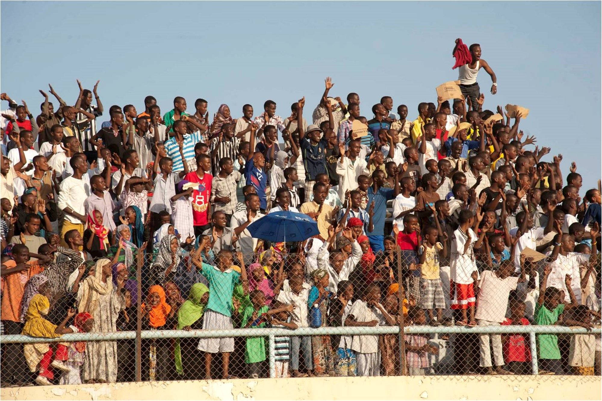 Mozambique 桌布 壁紙 — 一群充滿活力的人擠在鐵絲網圍欄後面，在晴朗的藍天下熱情歡呼。