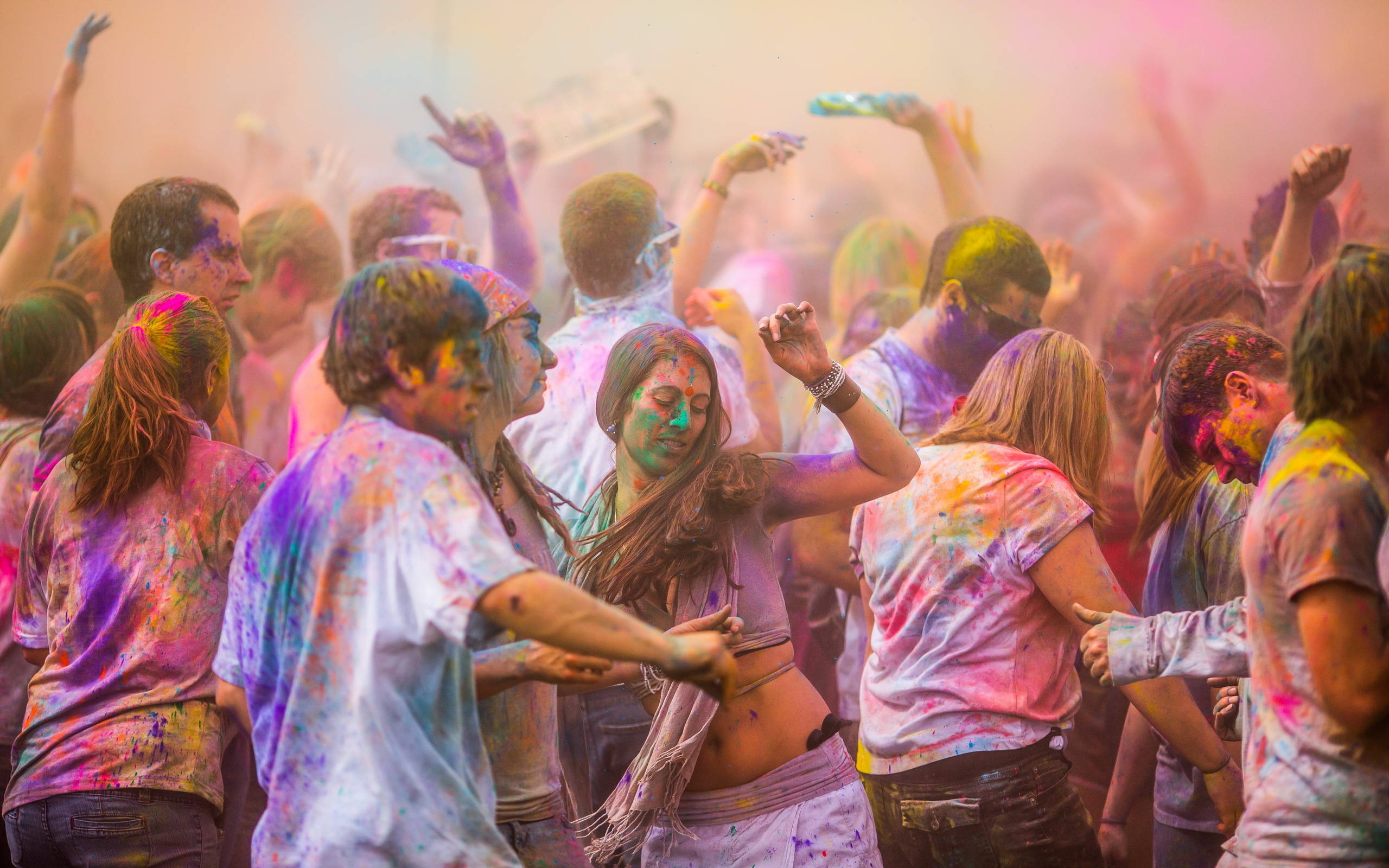 Holi 桌布 壁紙 — 一群充滿活力的人群在節日慶祝中，興奮地舉起雙臂，身上覆蓋著五彩粉末，歡快地跳舞。