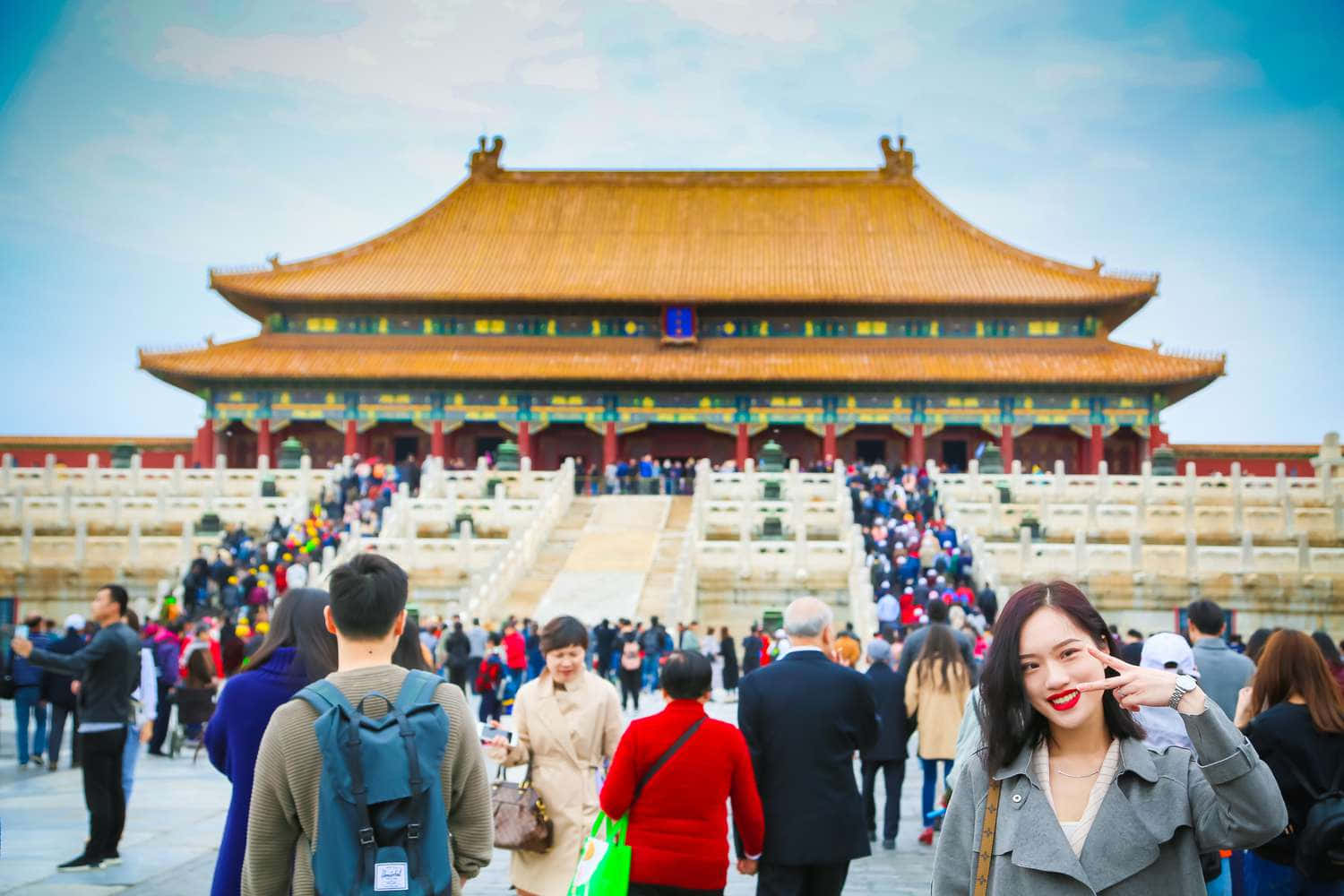 中文 桌布 壁紙 — 一群充滿活力的人群聚集在宏偉的傳統中國宮殿前，宮殿擁有金色屋頂瓦片，背景是清澈的藍天。