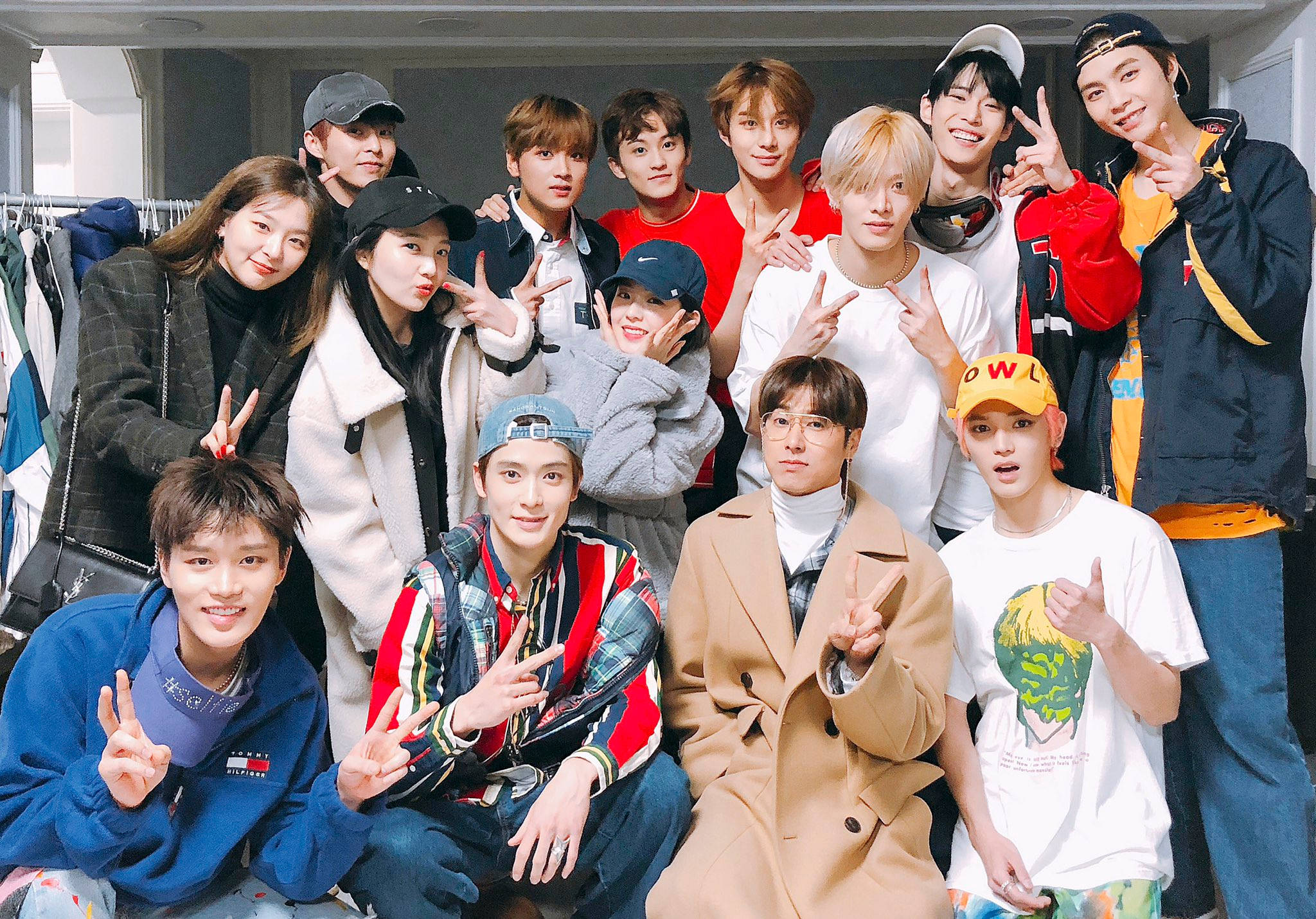 Nct 桌布 壁紙 — 一群充滿活力的年輕人在服裝店裡一起擺出和平手勢，在自然光下燦爛微笑。