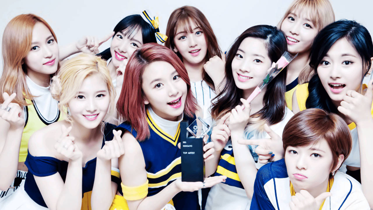 twice 桌布 壁紙 — 一群充滿活力的年輕女性穿著藍色和黃色的啦啦隊服裝，在純白色背景前開心地拿著獎盃擺姿勢。