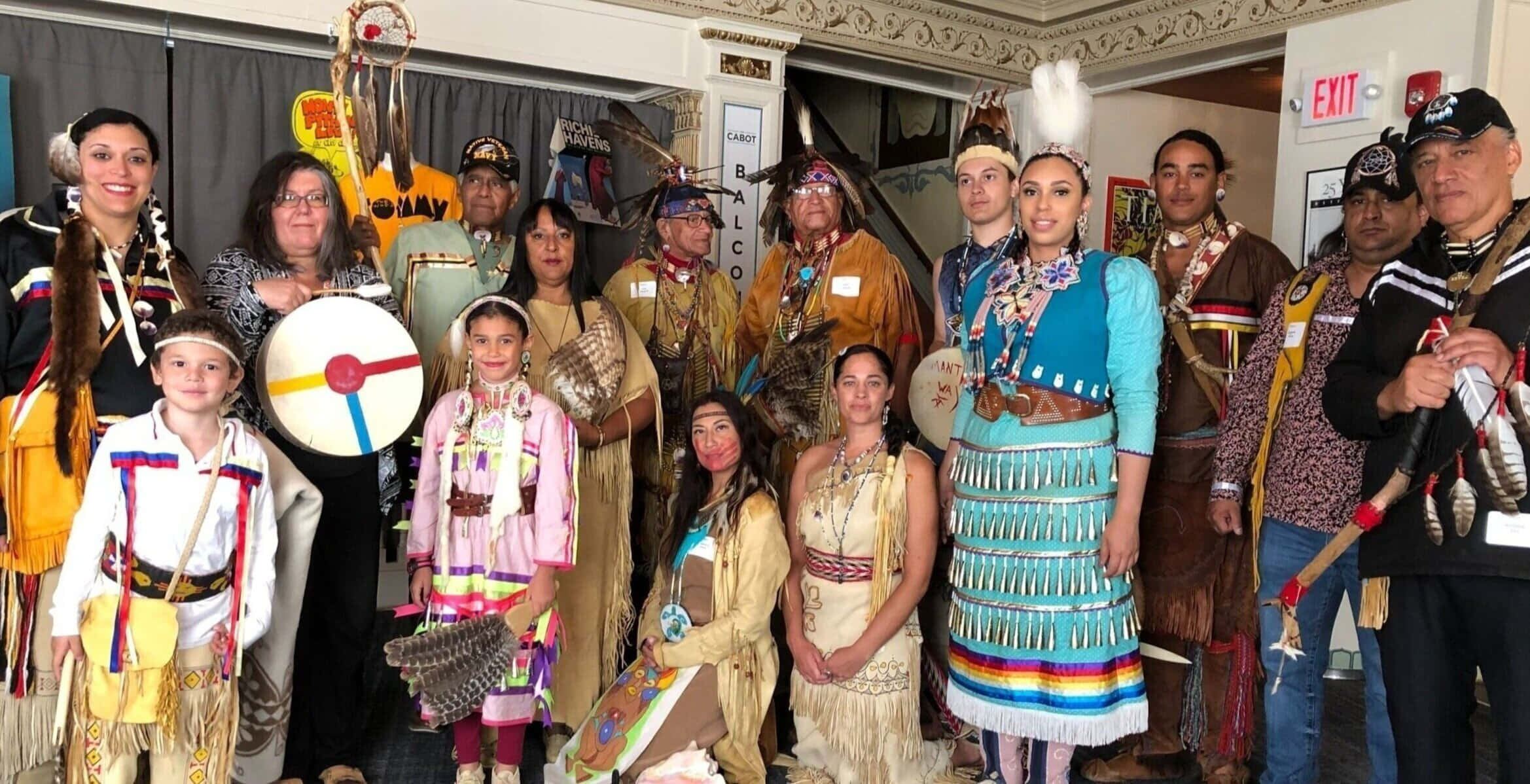 Native American 桌布 壁紙 — 一群充滿活力的美洲原住民穿著傳統服飾，手持鼓和儀式用品，在室內一起擺姿勢。