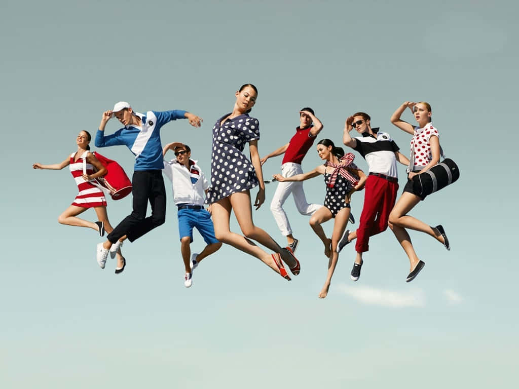 Clothing Design 桌布 壁紙 — 一群八個穿著時尚的人在空中跳躍，背景是晴朗的淡藍色天空。