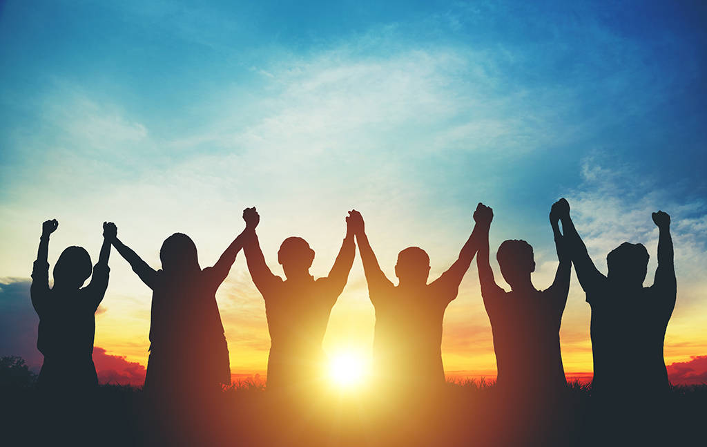 Teamwork 桌布 壁紙 — 一群剪影人物手牽手、高舉手臂，在充滿活力的日落天空下團結一致。