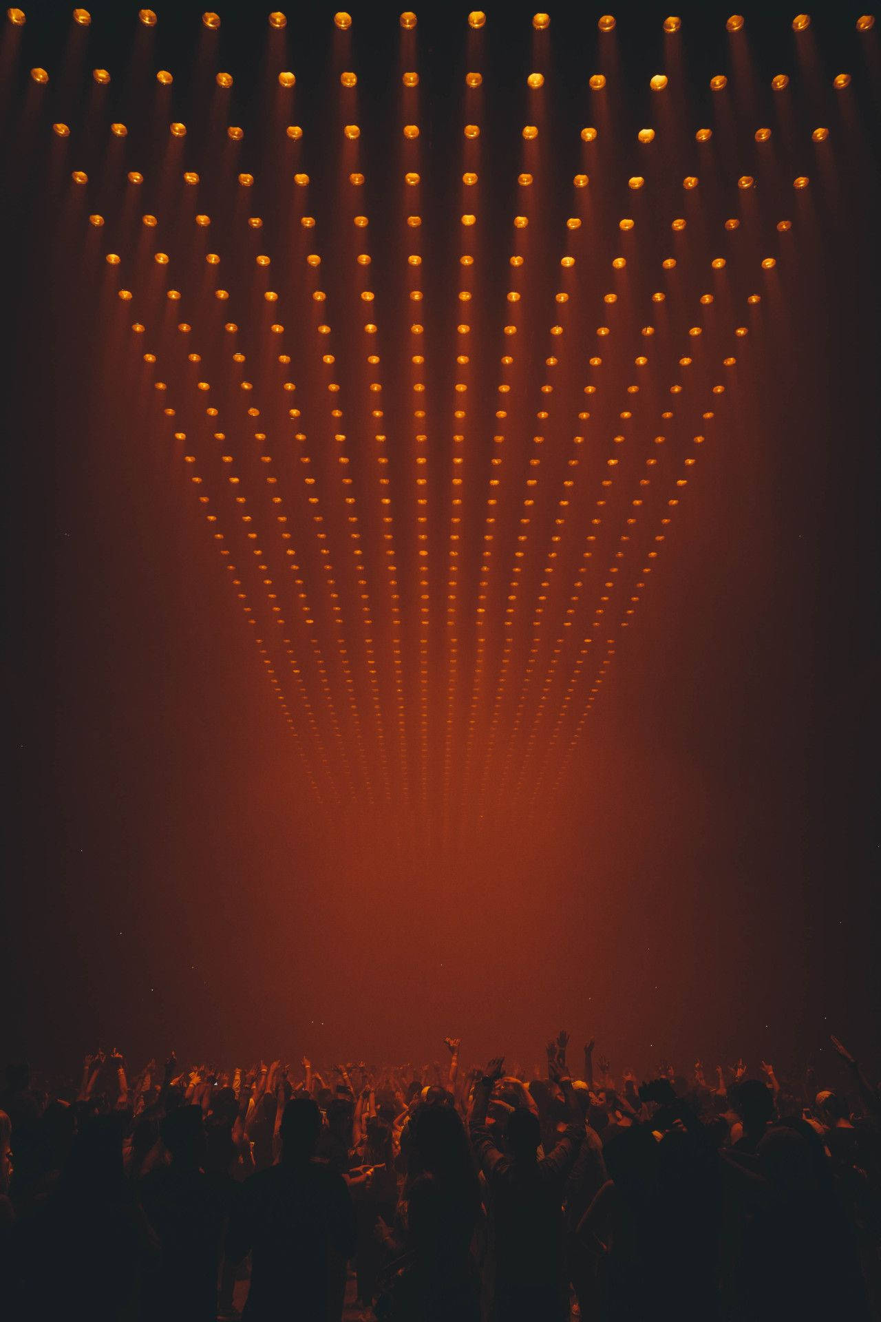 kanye west android 桌布 壁紙 — 一群剪影般的演唱會觀眾在溫暖橙色舞台燈光的耀眼天幕下舉起雙手。