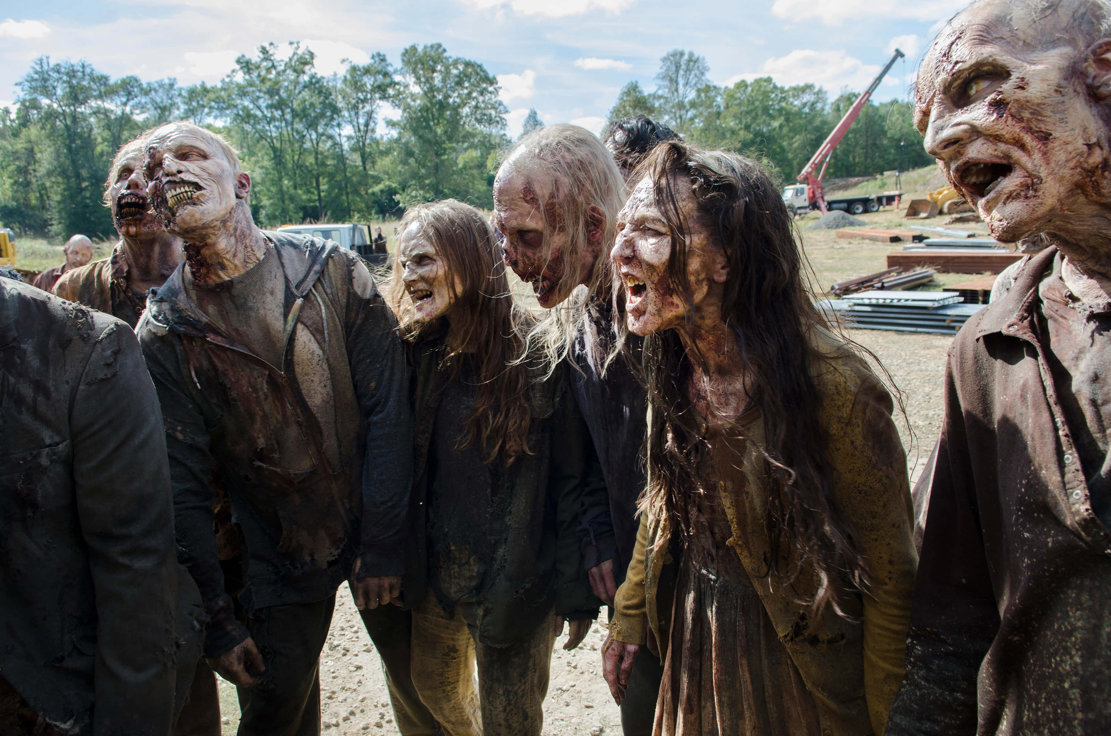 zombies 桌布 壁紙 — 一群可怕、腐爛的殭屍，衣衫襤褸，滿臉鮮血，在陽光普照、塵土飛揚的建築工地蹣跚前行。
