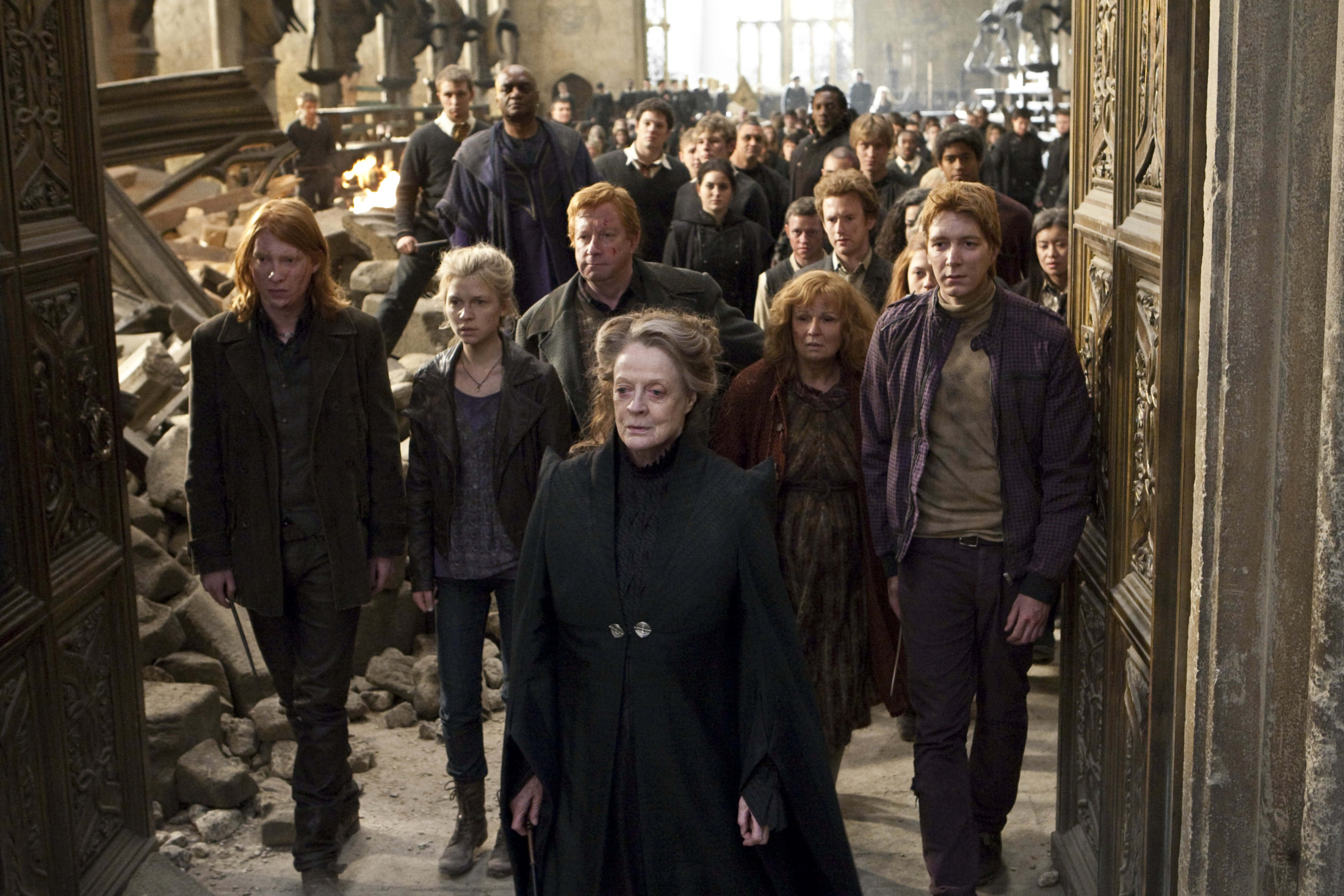 The Battle Of Hogwarts 桌布 壁紙 — 一群堅定的角色走過一個廢墟般的大廳，滿佈瓦礫和華麗的門。