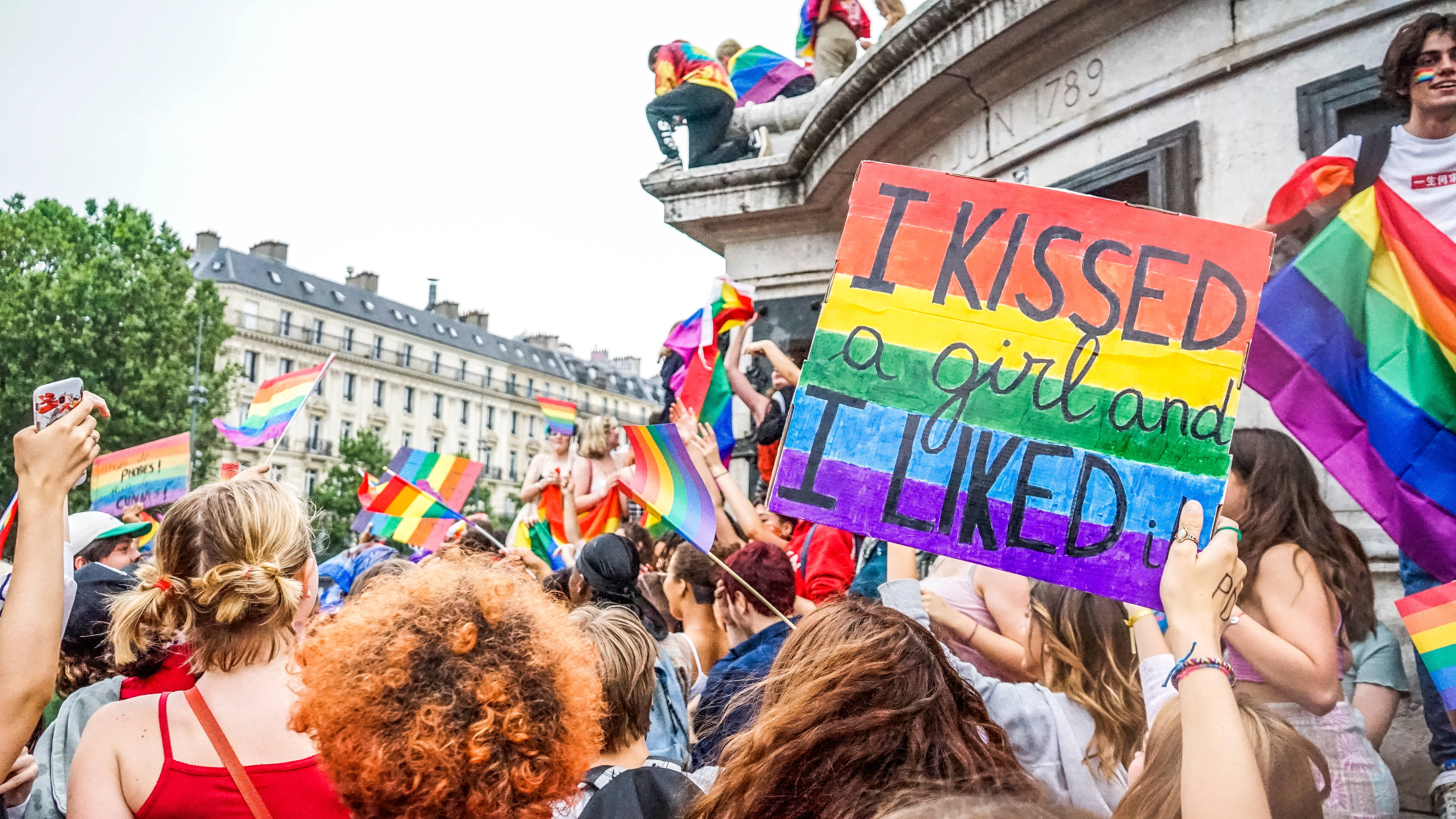 女同志 桌布 壁紙 — 一群多元人士在Pride活動中揮舞彩虹旗和手持手製標語牌，上面寫著「I kissed a girl and I liked it」慶祝。