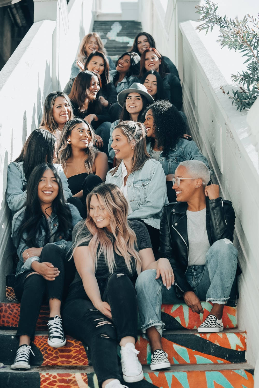 Friendship 桌布 壁紙 — 一群多元化的年輕女性在明亮的日光下，隨意地坐在色彩鮮豔的戶外樓梯上微笑。