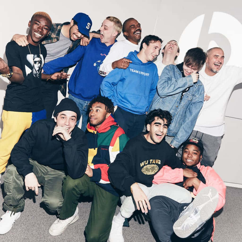 Brockhampton 桌布 壁紙 — 一群多元化的年輕男性在光線明亮的室內攝影棚中，身後牆上有一個大型白色標誌，他們笑著並充滿活力地擺姿勢。
