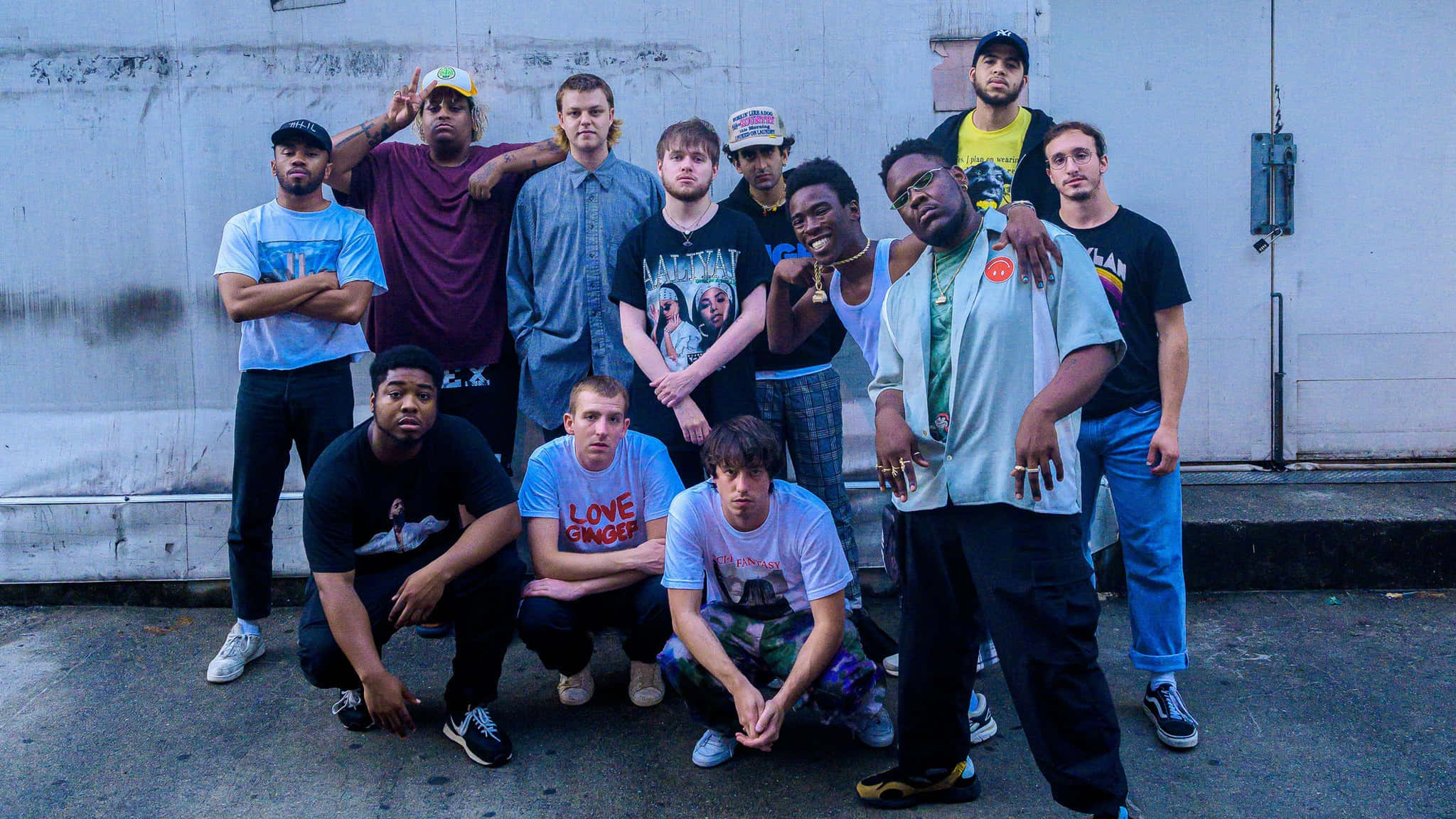 Brockhampton 桌布 壁紙 — 一群多元化的年輕男性穿著休閒街頭服飾，在柔和日光下自信地靠著風化的城市牆壁擺姿勢。