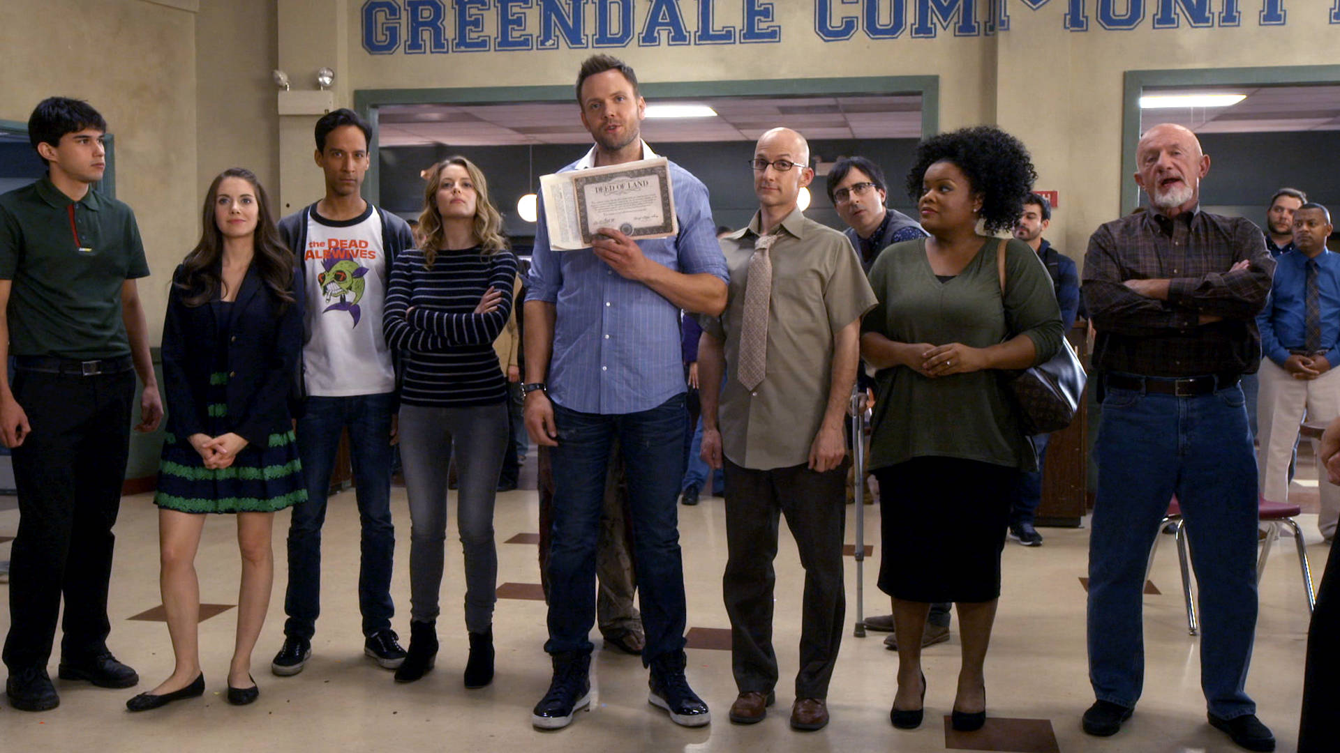 社群 桌布 壁紙 — 一群多元化的成年人站在學校走廊，上方有「Greendale Community」標誌，一名男子手持裱框證書，其他人則在觀看。