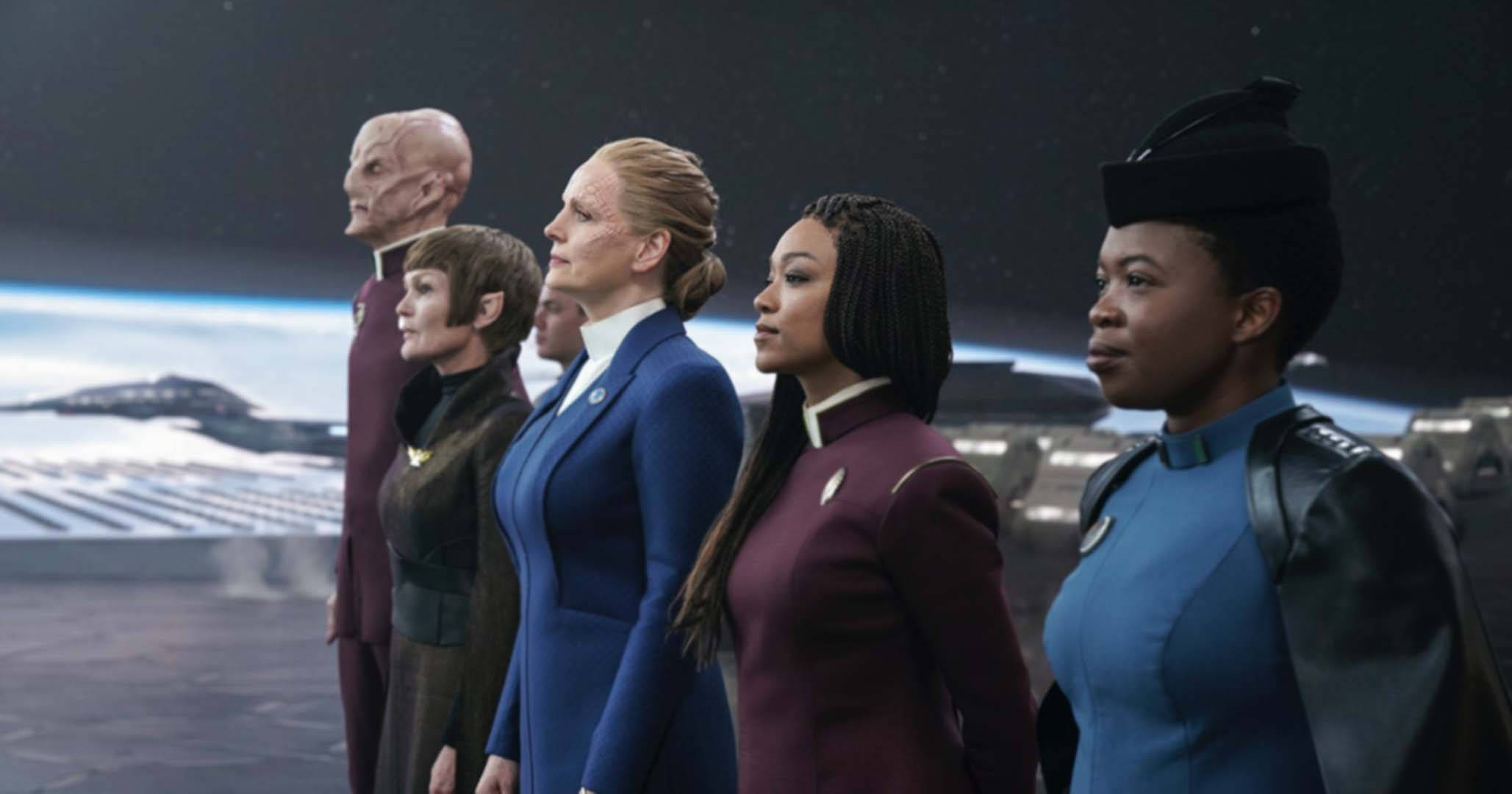 Discovery 桌布 壁紙 — 一群多元化的船員穿著星際艦隊制服，在星艦艦橋上以側面姿態站立，俯瞰一個雪行星和星域。