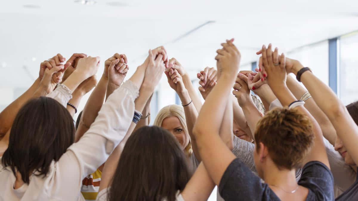 Teamwork 桌布 壁紙 — 一群多元背景的人們在室內圍成圓圈手牽手，形成一條團結的人鏈，臉上洋溢著喜悅。