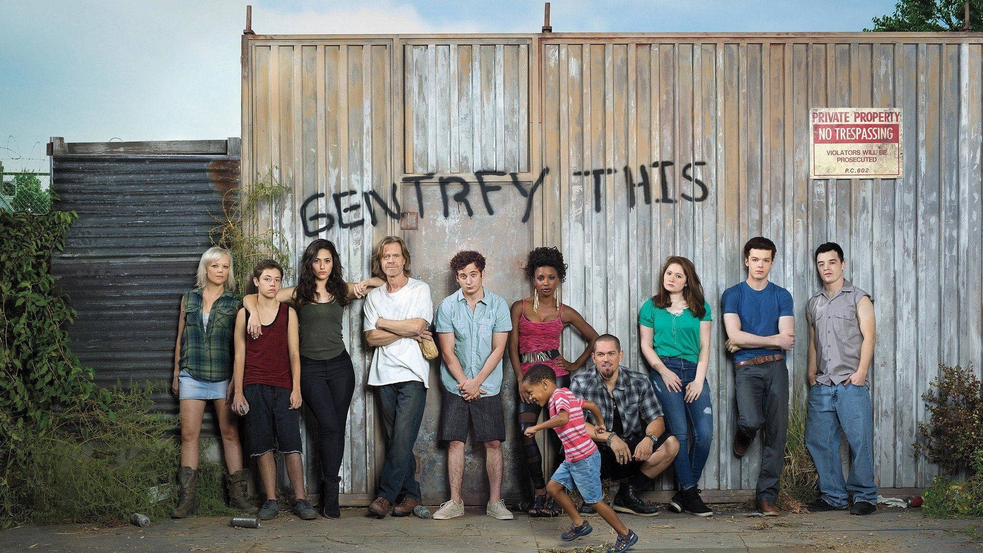 Family 桌布 壁紙 — 一群多元背景的人在一片晴朗天空下，在一個寫有「GENTRIFY THIS」塗鴉的風化木柵欄前擺姿勢。