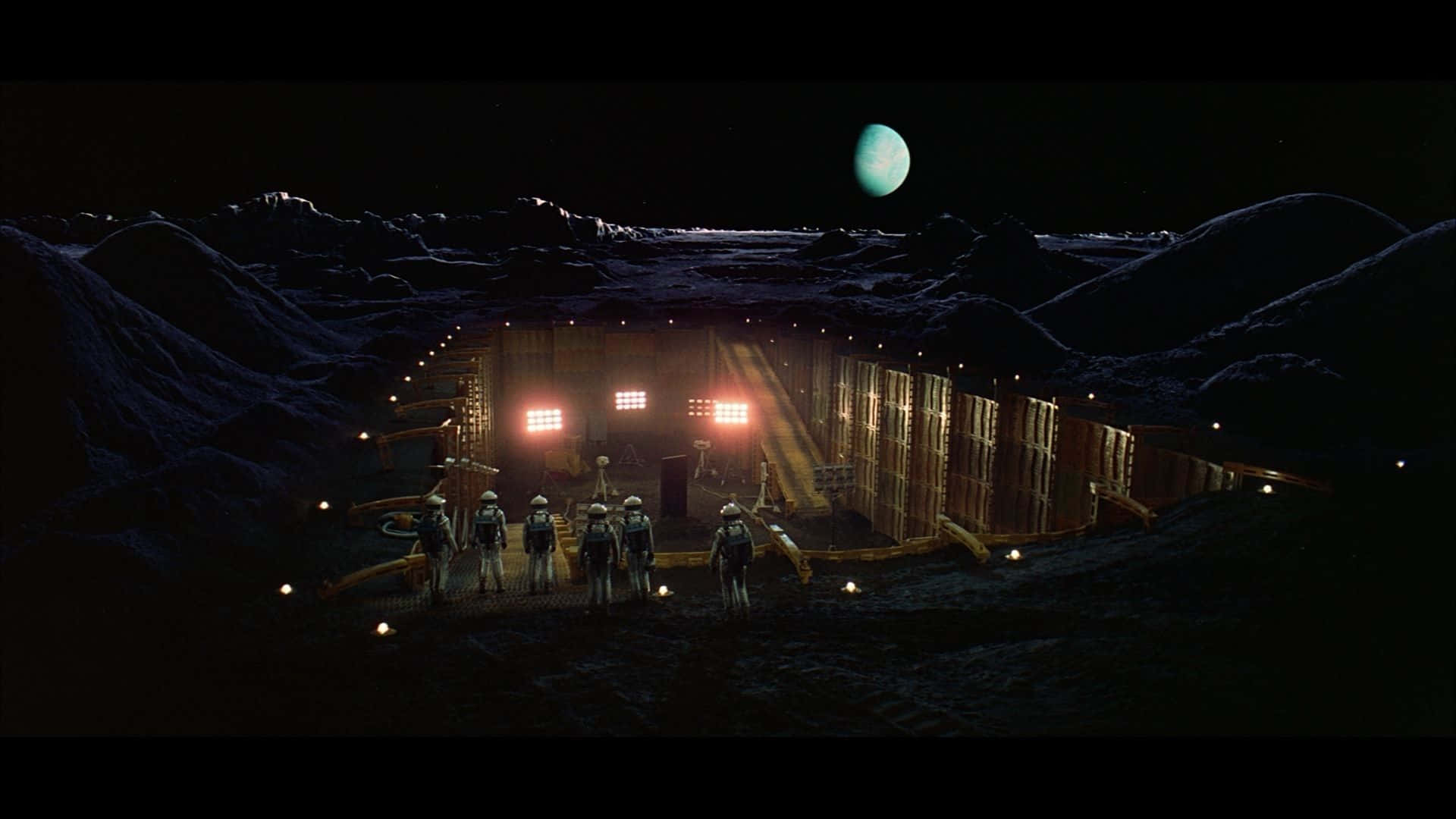 2001 A Space Odyssey 桌布 壁紙 — 一群太空人站在一個荒涼的外星衛星上，在淡綠色月亮下，面對一個發光的地下設施。