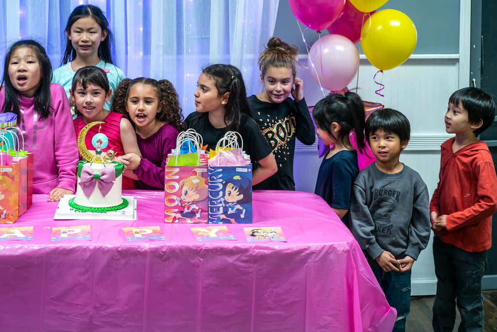 Birthday Party 桌布 壁紙 — 一群孩子圍著一張粉紅色的桌子，上面有生日蛋糕和氣球，在室內進行節日慶祝。