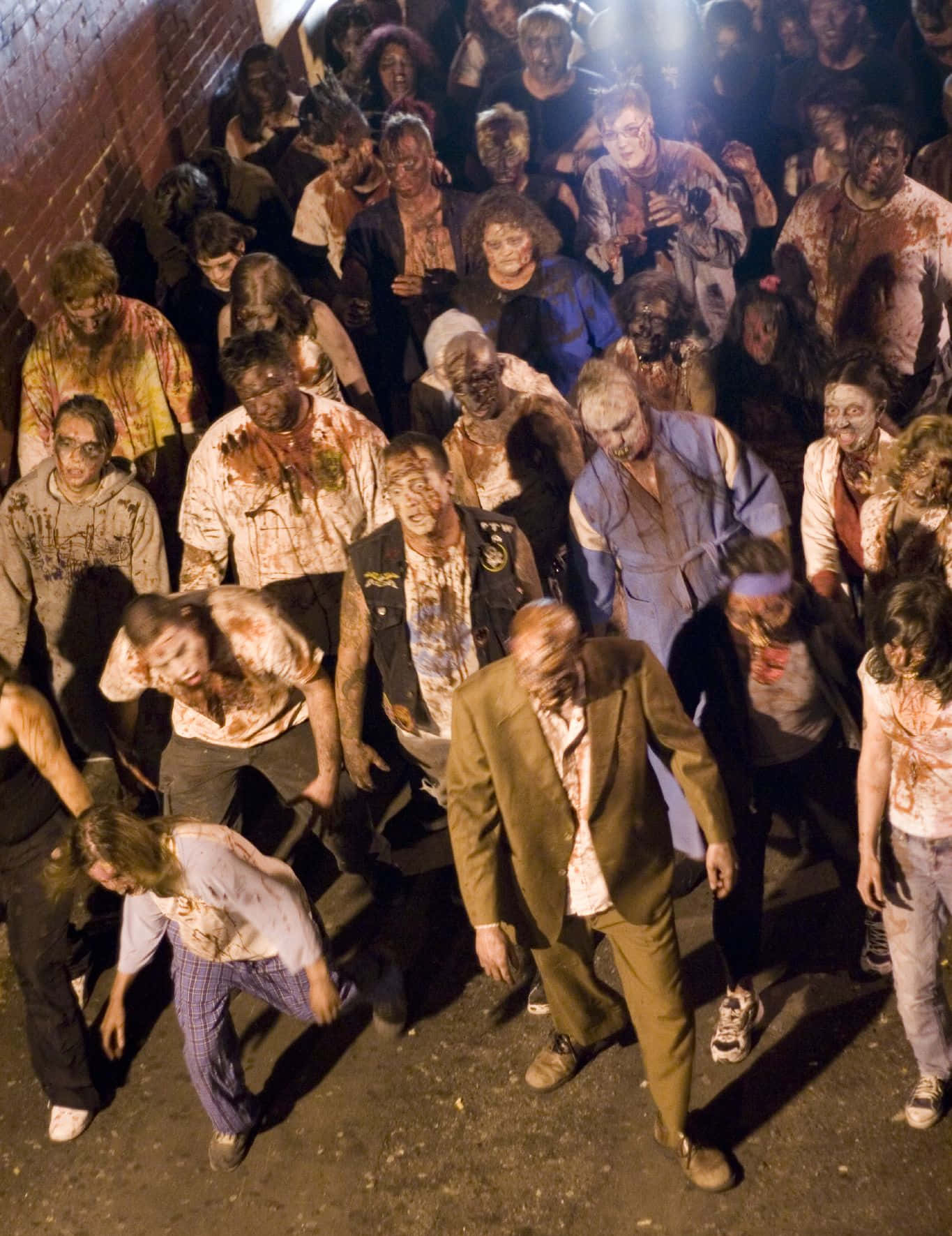 Zombie Apocalypse 桌布 壁紙 — 一群密集的恐怖、血淋淋的殭屍在昏暗的後巷中，在刺眼的人造燈光下蹣跚前行。