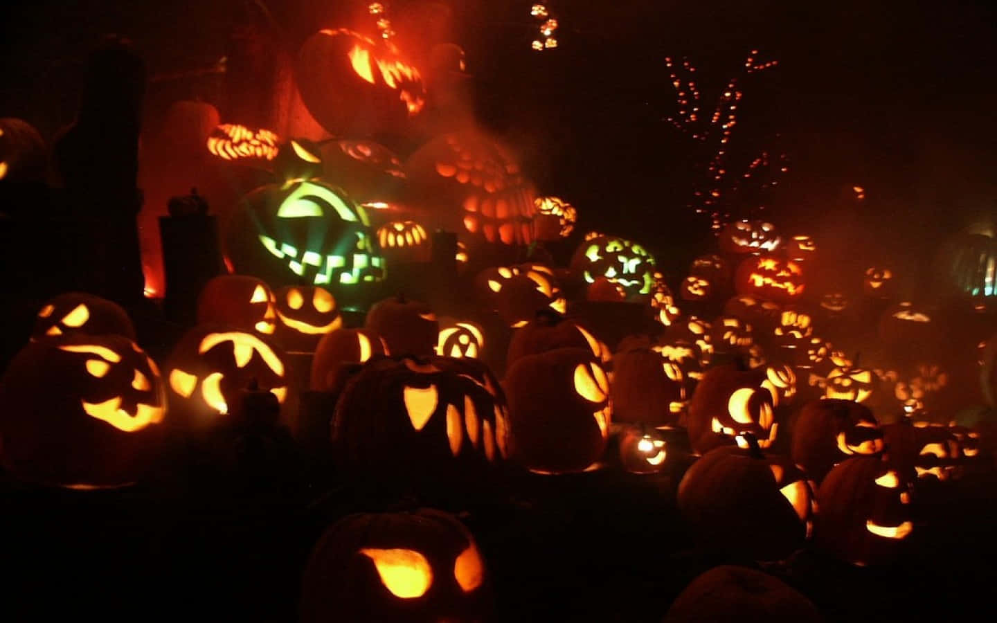 Jack O Lantern 桌布 壁紙 — 一群密集的發光傑克南瓜燈，帶有各種恐怖面孔，照亮了黑暗迷霧的萬聖節場景。