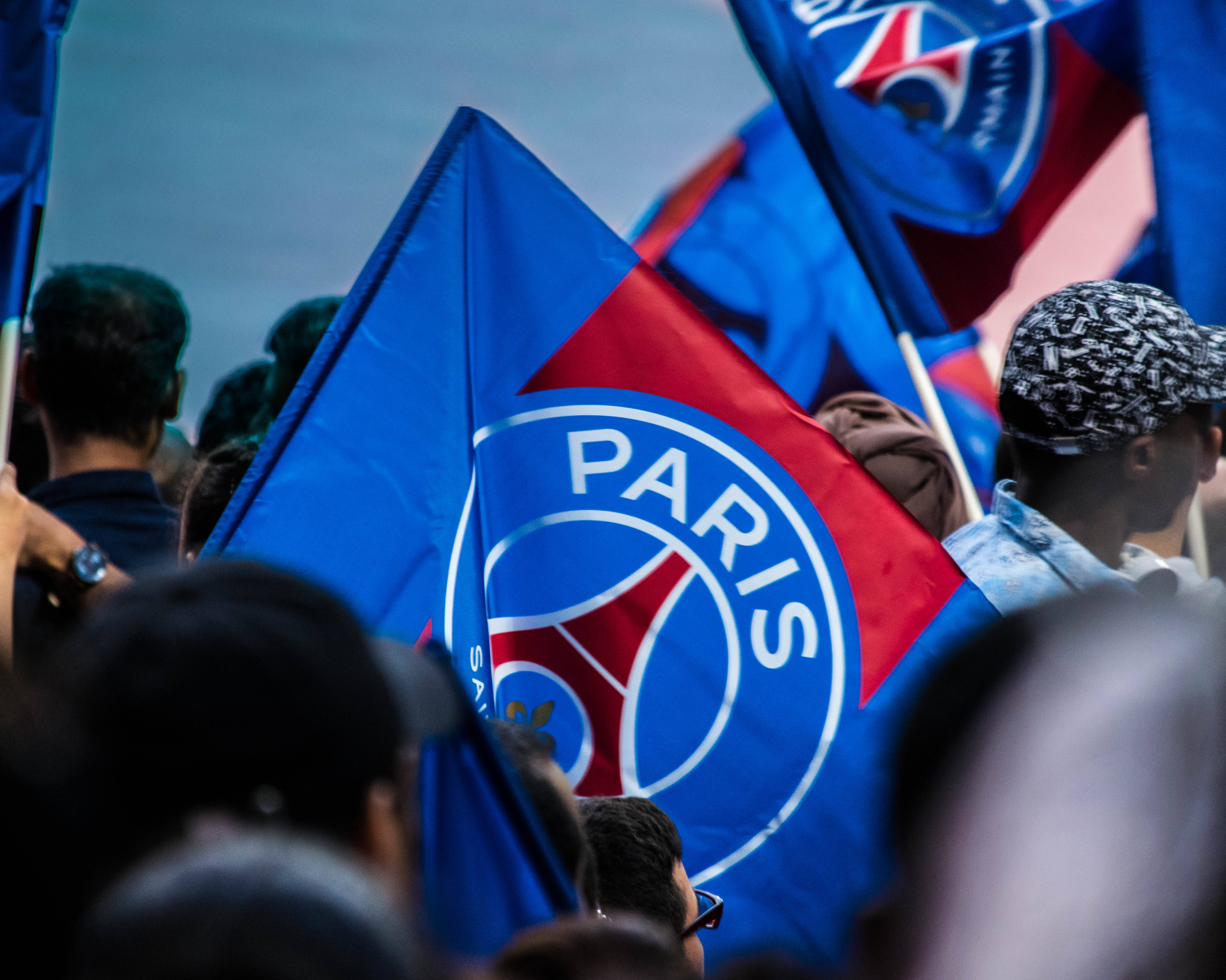 梅西 PSG 桌布 壁紙 — 一群巴黎聖日耳曼球迷在陰天揮舞著藍色和紅色的球隊旗幟。