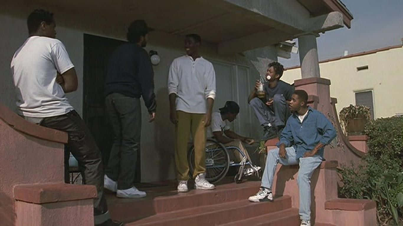 Boyz N The Hood 桌布 壁紙 — 一群年輕男子在明亮的日光下聚集在房屋門廊的粉紅色混凝土台階上。