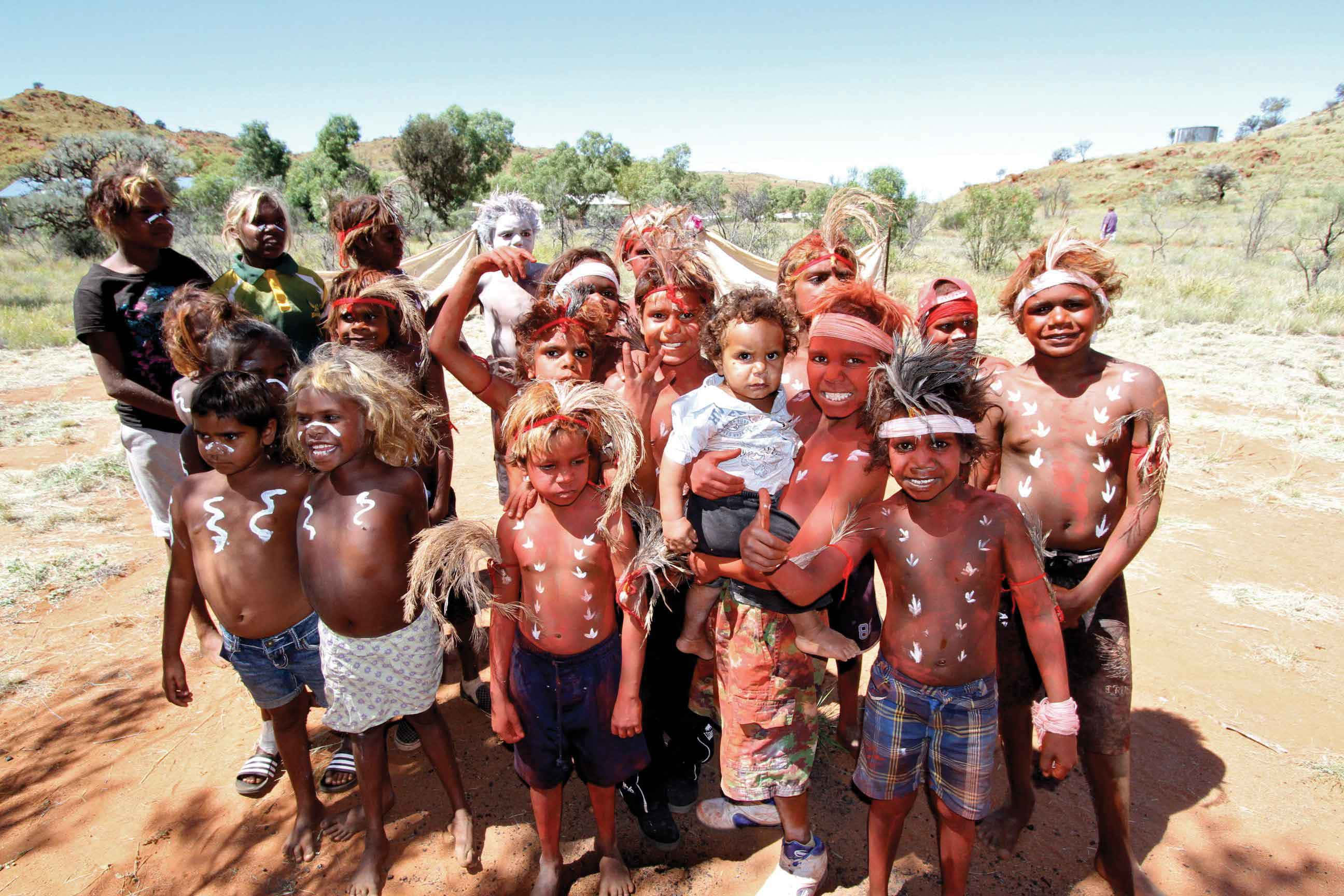 Aboriginal 桌布 壁紙 — 一群快樂的原住民兒童和成人，身上畫著傳統彩繪，在陽光明媚的乾旱景觀中一起擺姿勢。