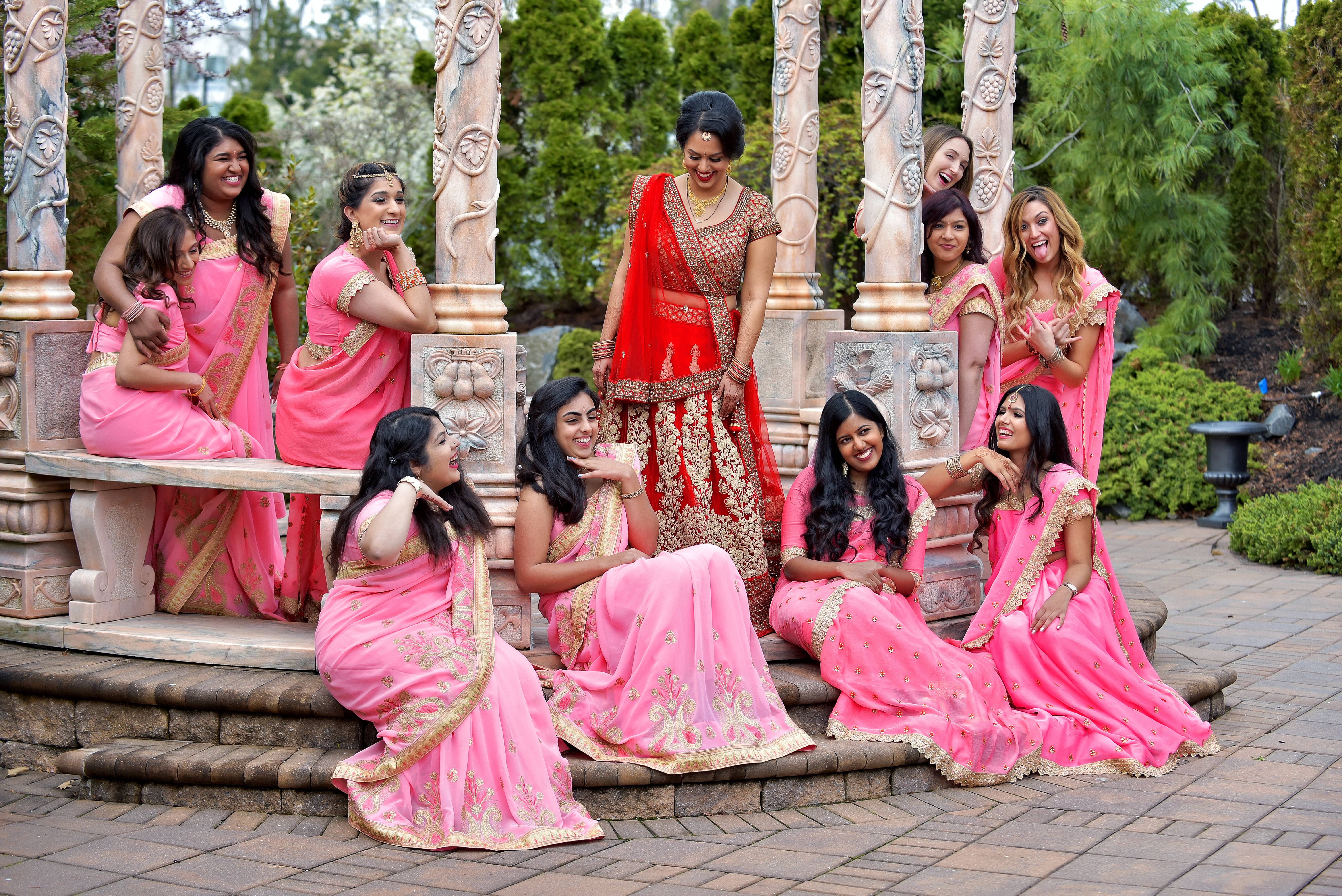 Bridesmaids 桌布 壁紙 — 一群快樂的女性穿著鮮豔的粉紅色和紅色傳統服飾，在一個被茂密綠植環繞的石亭中一起擺姿勢。