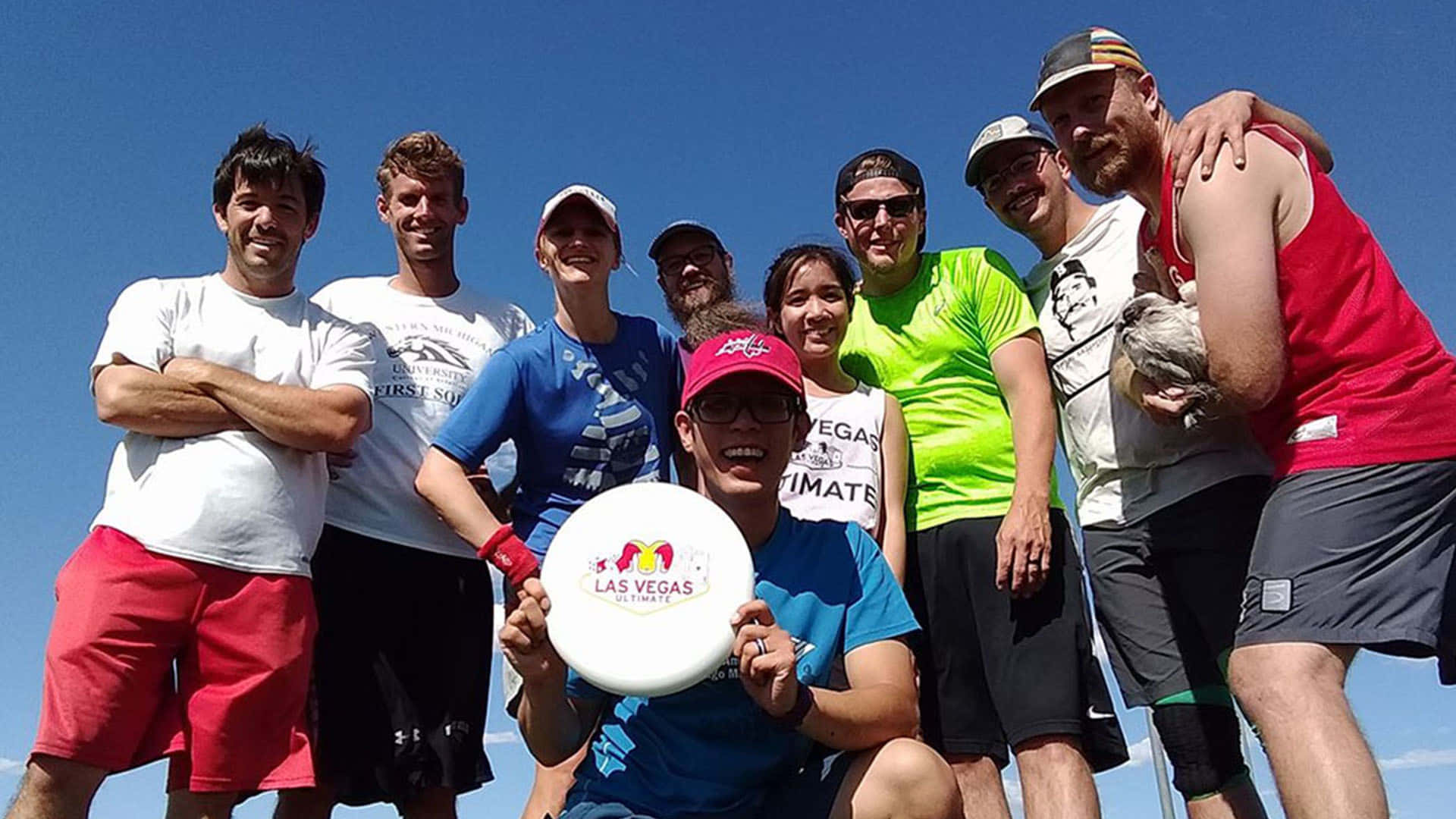 Frisbee 桌布 壁紙 — 一群快樂的飛盤玩家在晴朗的藍天下戶外擺姿勢，其中一人手持拉斯維加斯飛盤。