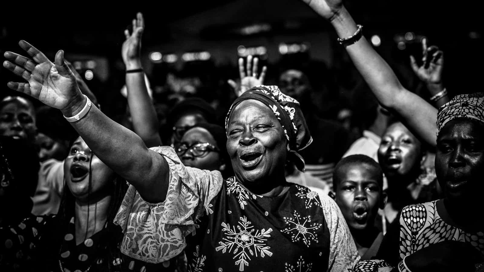 Nigeria 桌布 壁紙 — 一群快樂的黑白人群在昏暗的舞台燈光下舉手進行狂喜的敬拜。